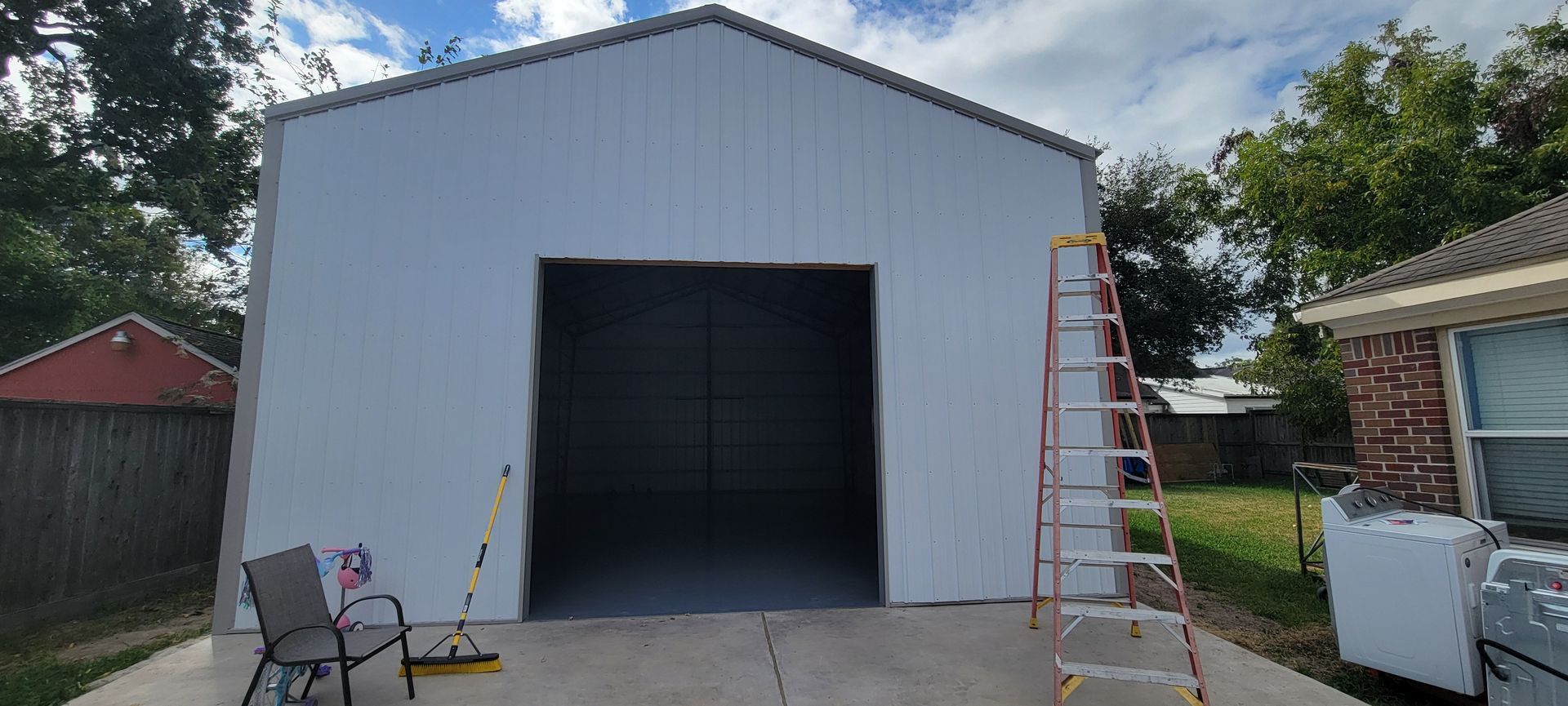 White metal garage with open door, a ladder, and a chair on the concrete driveway.