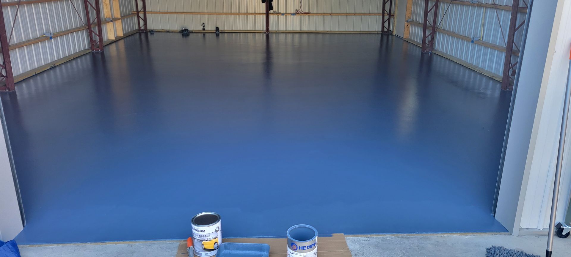 A recently painted dark blue garage floor with paint cans and tools visible.