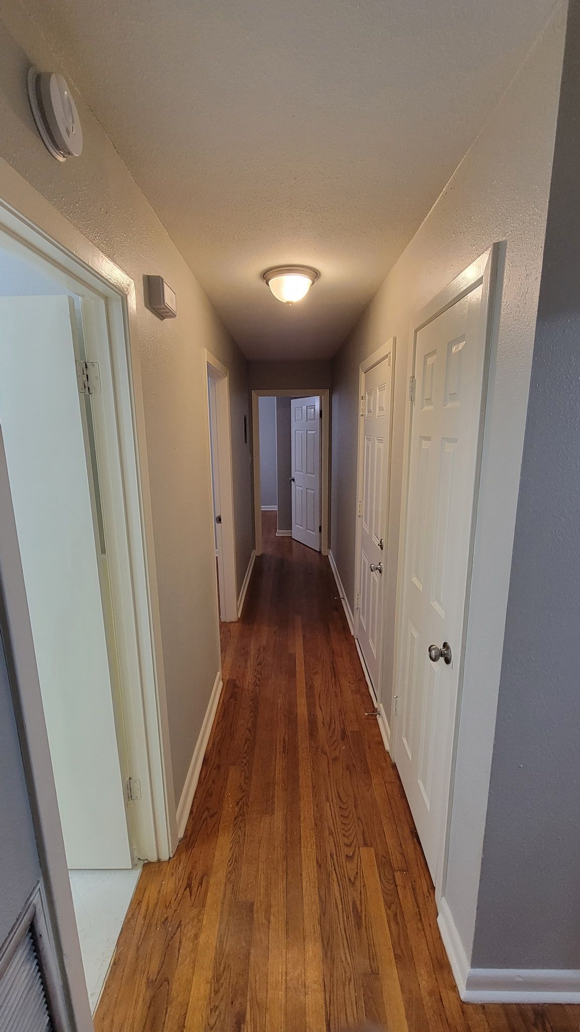 Narrow hallway with hardwood floors, white doors, and a ceiling light.