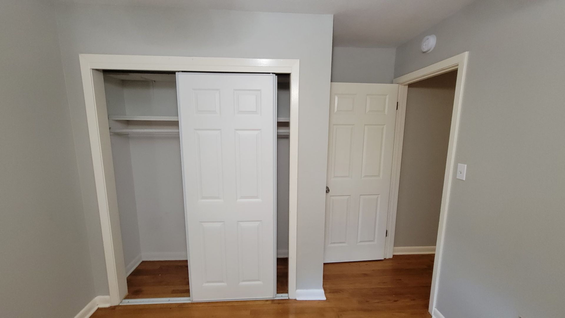 Empty bedroom interior with closet and door. White doors, gray walls, wood floor.