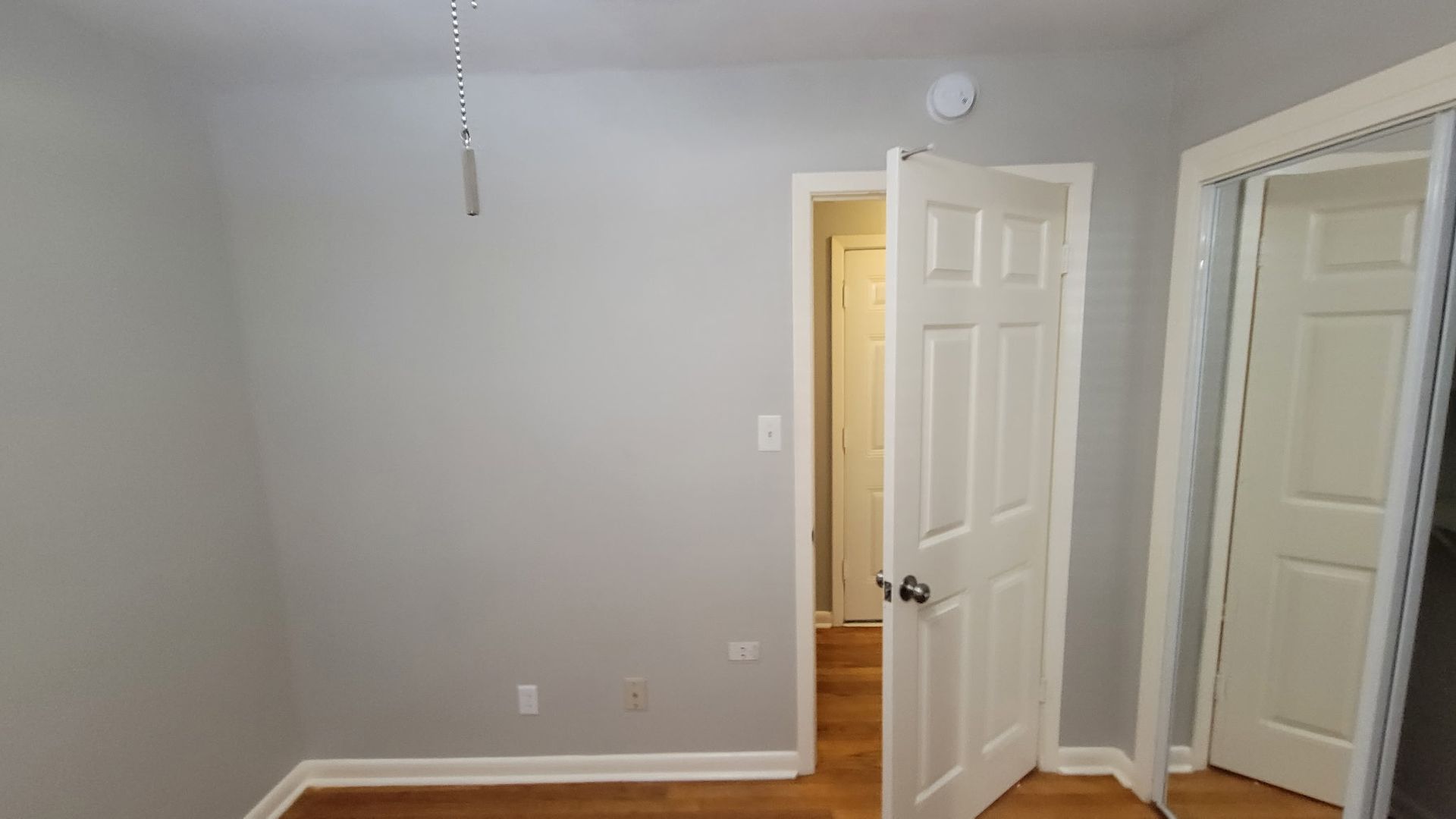 Empty bedroom with gray walls, white trim and doors, hardwood floor.
