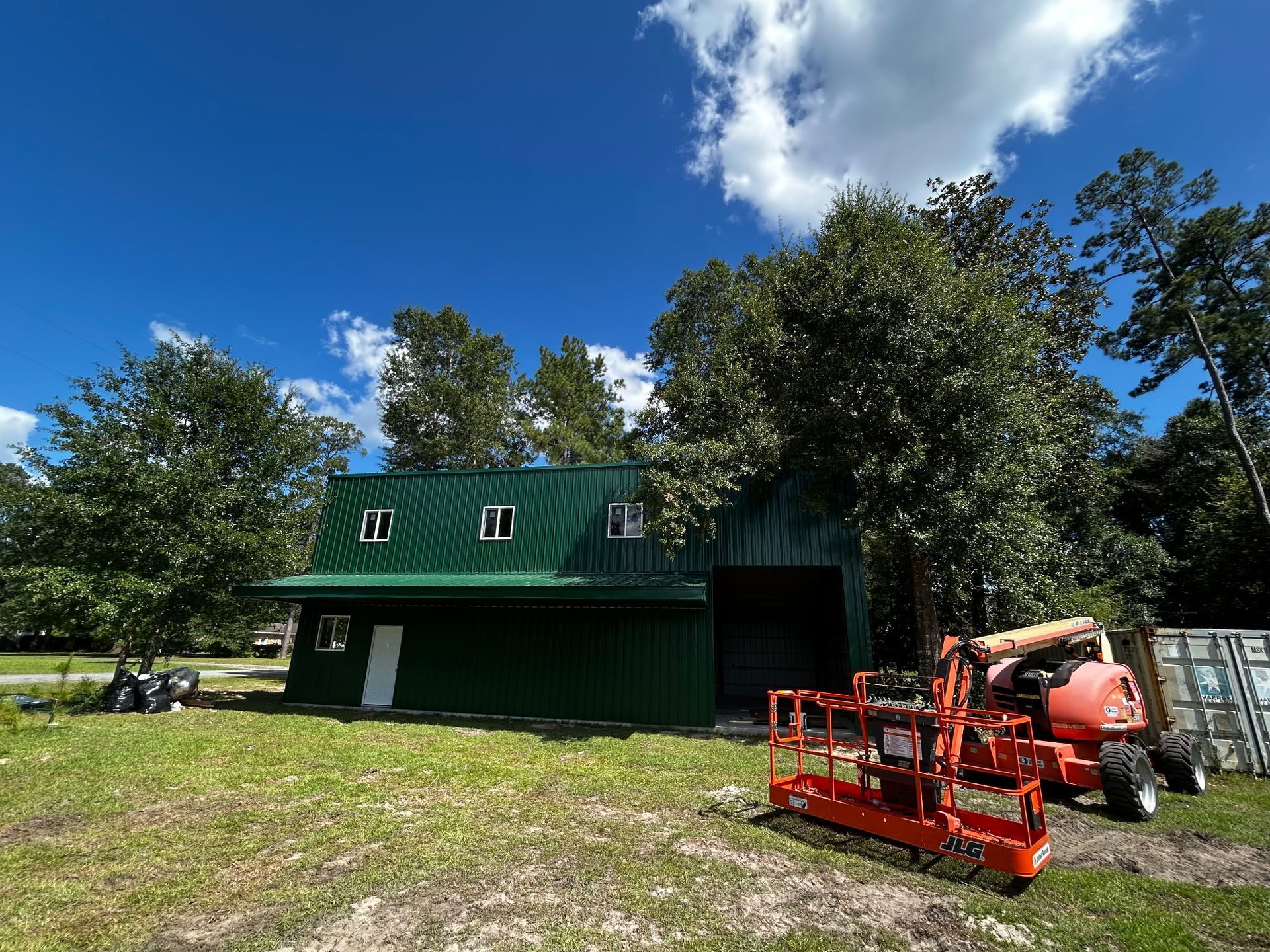 Green metal building with a lift in front on a sunny day.