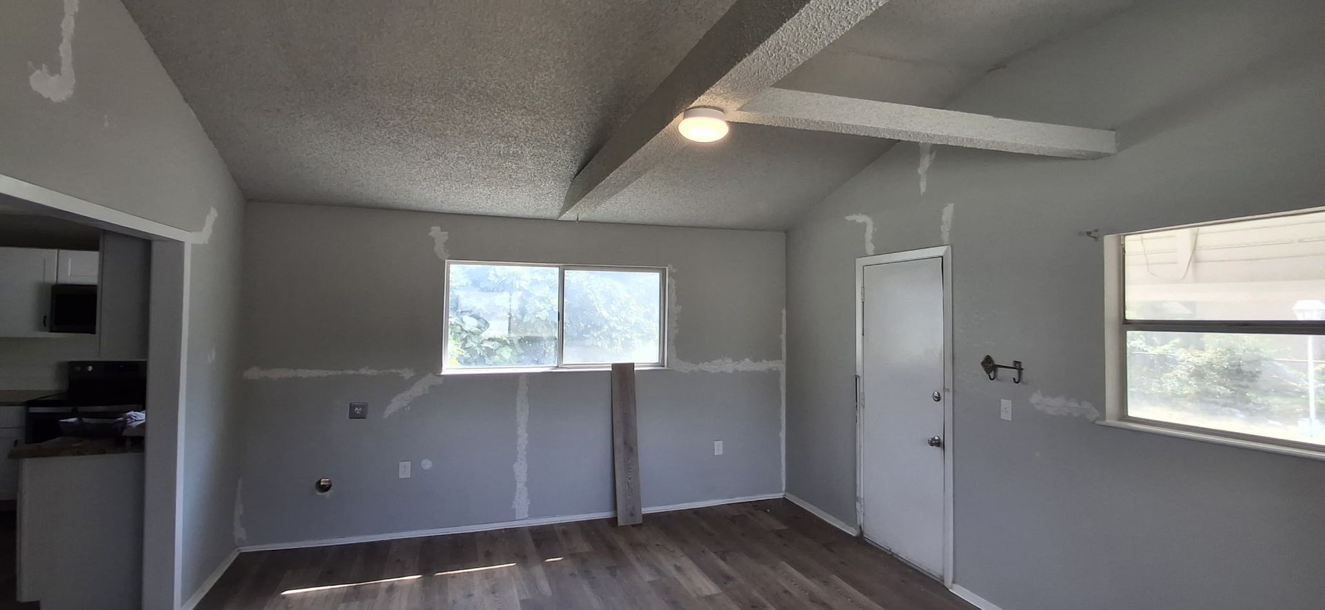 Interior view of a room under renovation with gray walls, a textured ceiling, and a wooden floor.