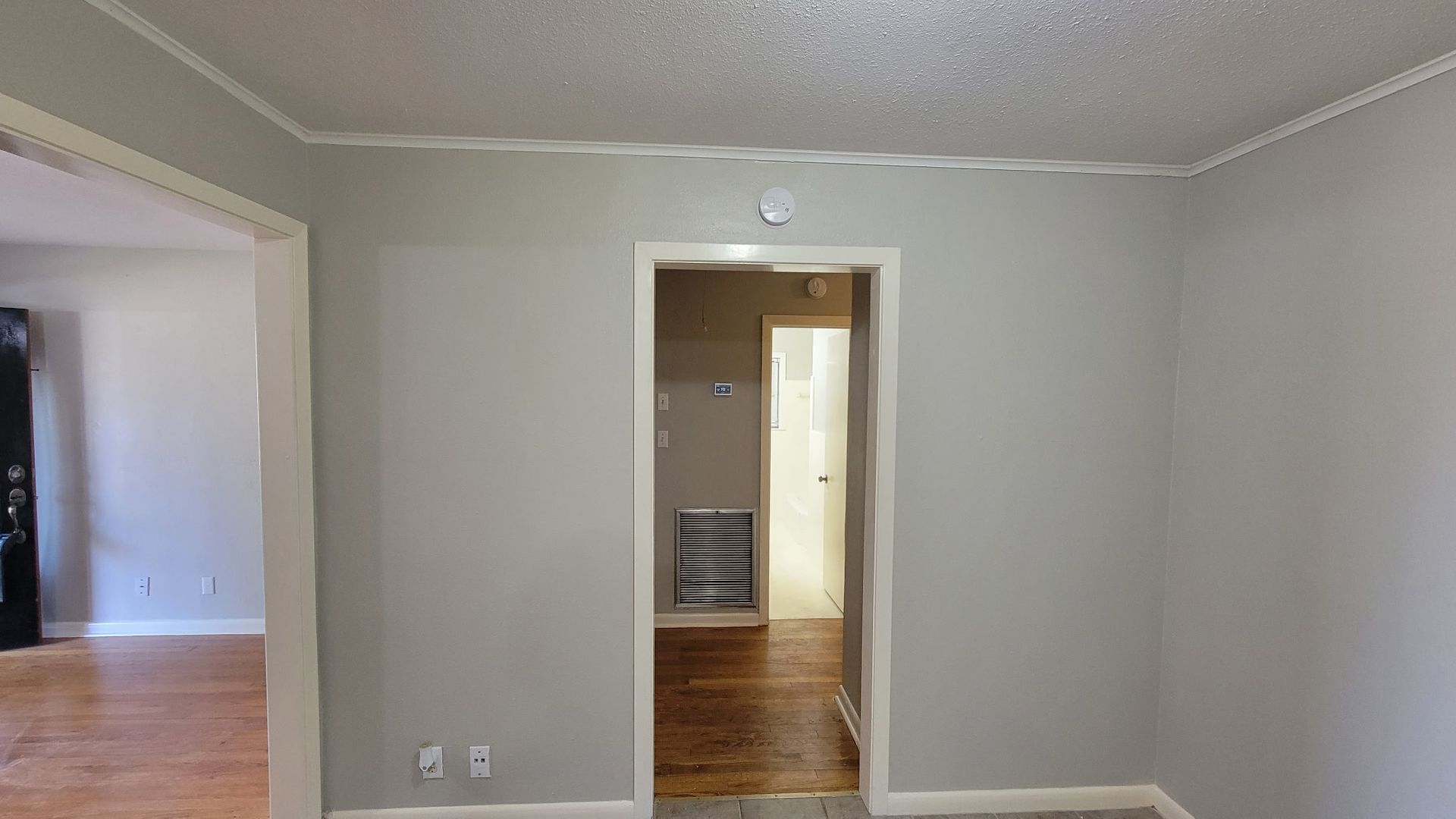 Gray-walled room with doorway leading to another room, trim around the ceiling and doorways.