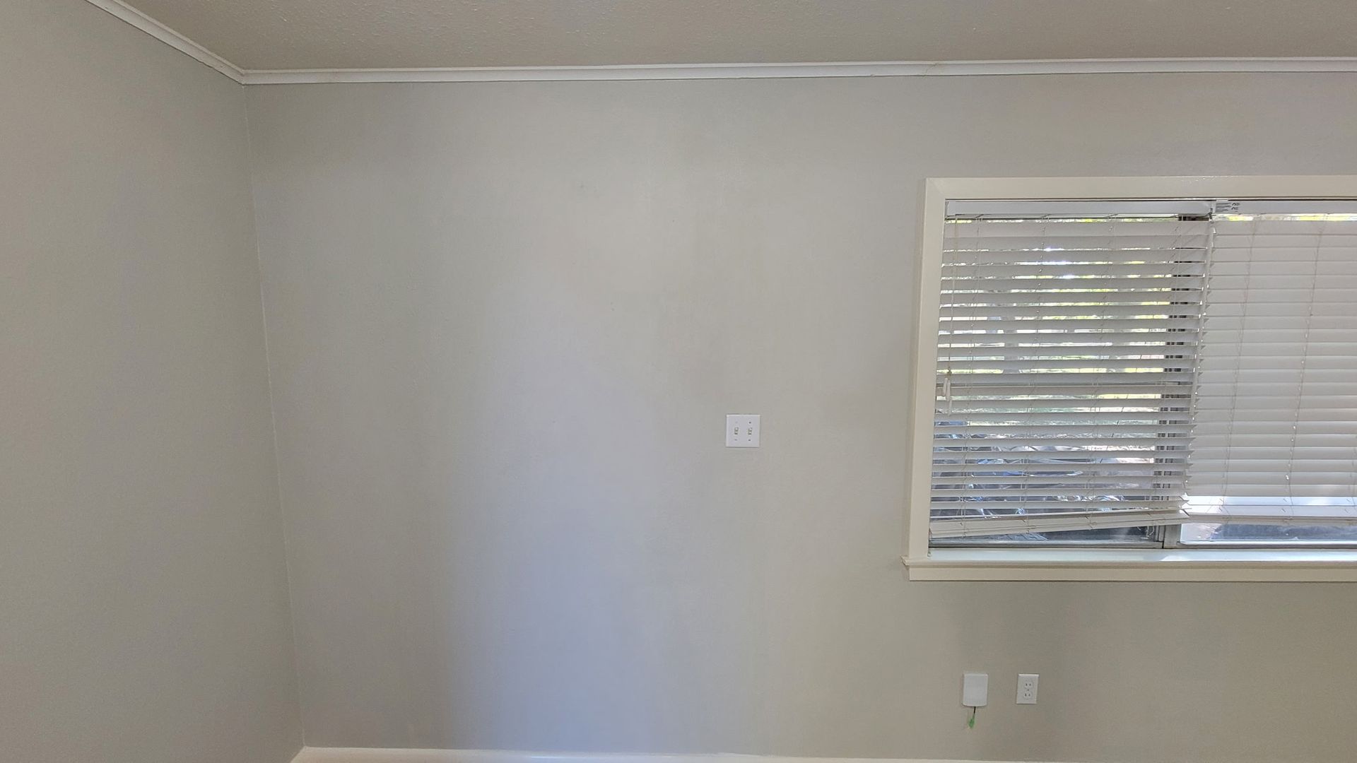 Empty room with light gray walls, white trim, and a window with closed blinds.