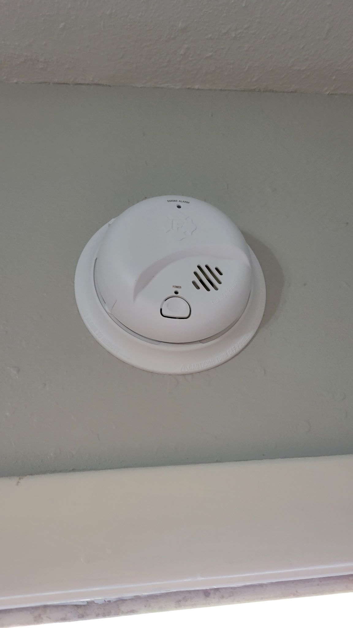 White smoke detector mounted on a gray wall near a white trim.