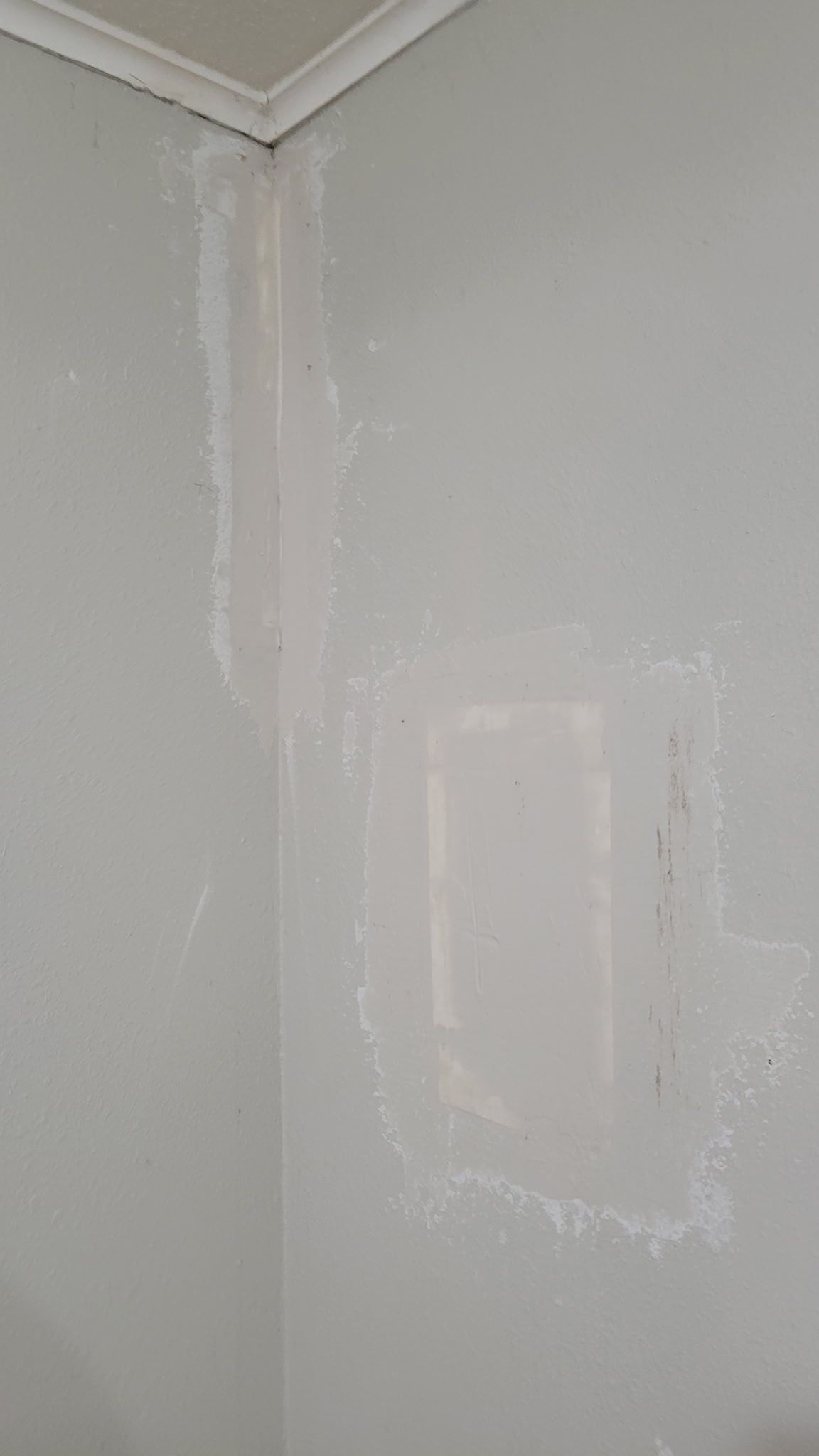 White painted wall with a rectangular patch of filler, adjacent to a corner with white trim; white residue around the patch.