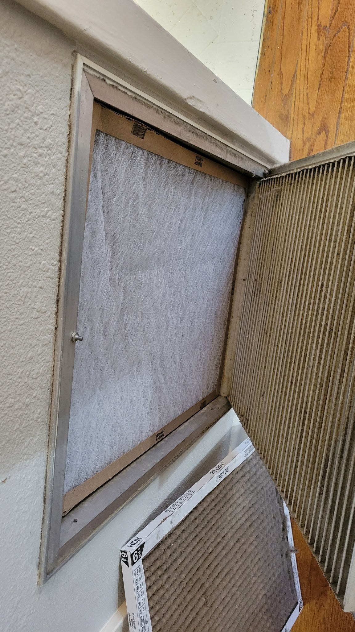 Open metal screen door with air filter in a stucco wall.