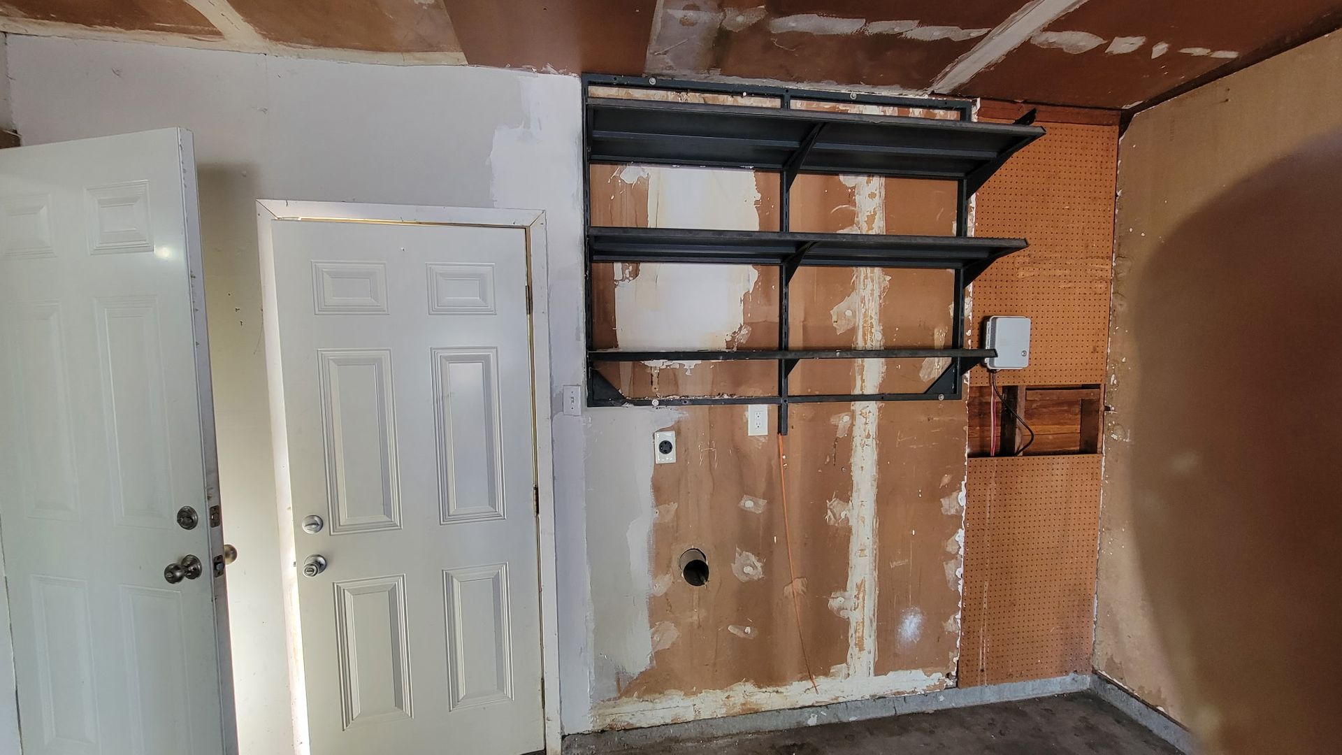 Room with a white door, shelving, and exposed wall studs, possibly under renovation.