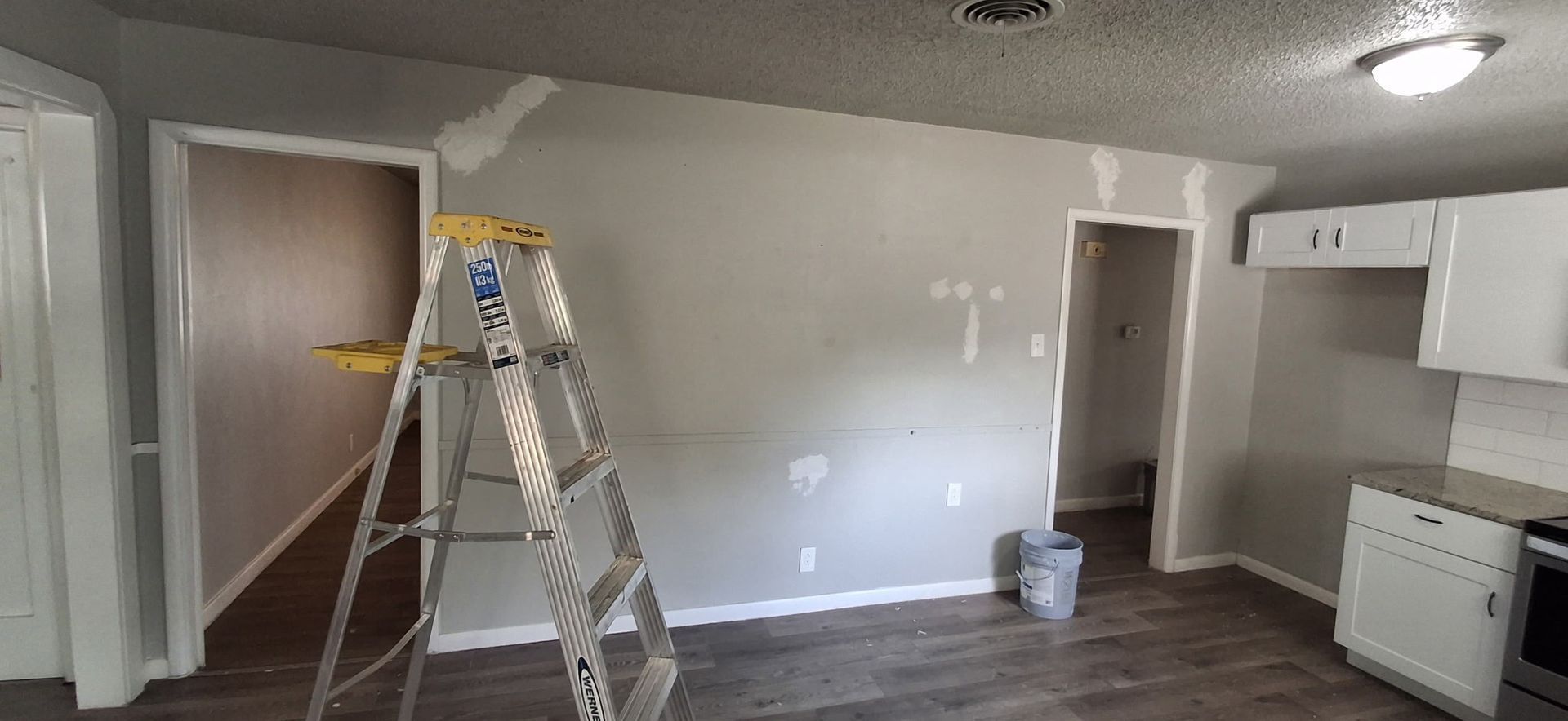 Interior room with ladder, freshly painted gray walls, kitchen cabinets, and dark wood flooring.