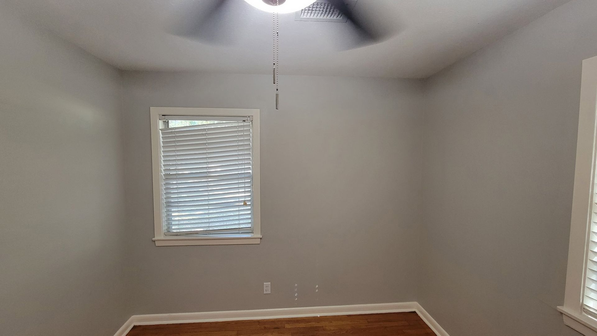 Empty room with gray walls, a window with blinds, and a ceiling fan.