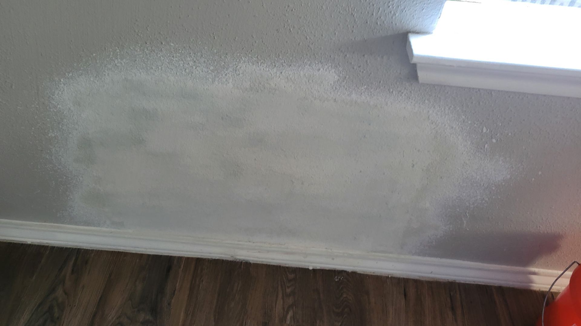 Gray wall with rectangular white patch, near a white window frame and baseboard.