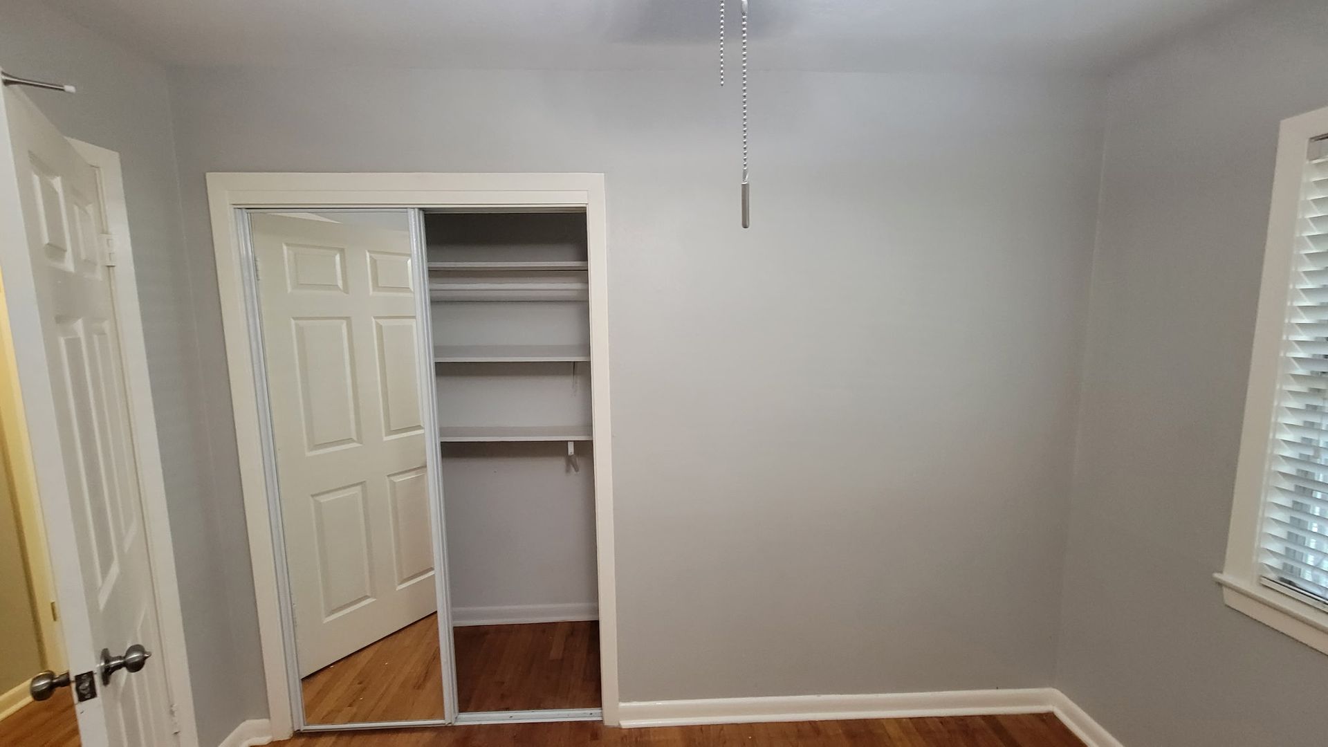 Empty room with a closet, door, and a window. Walls are gray, with hardwood floors and a white ceiling.
