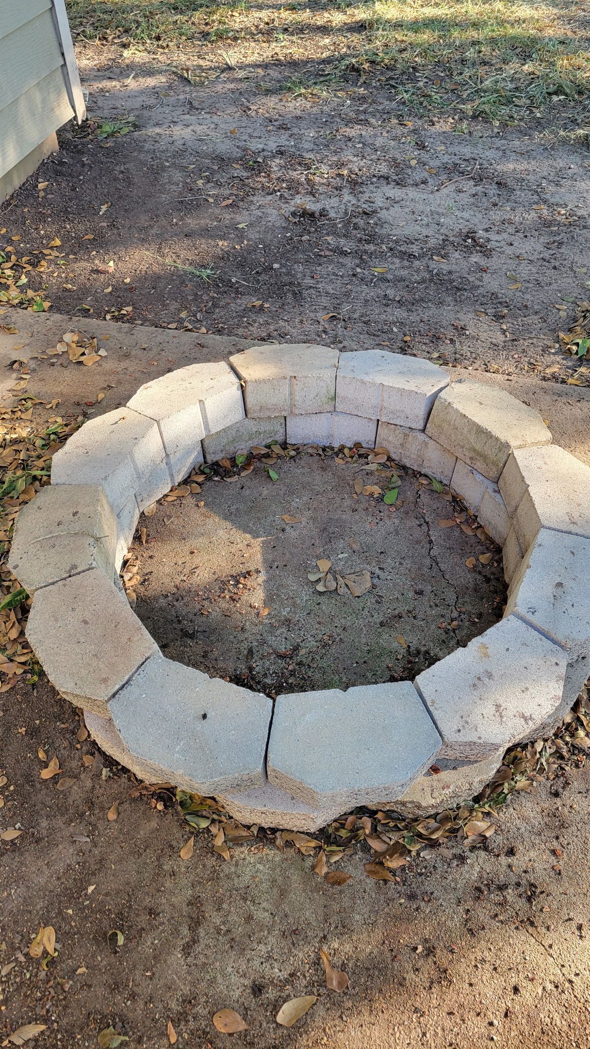 A circular fire pit made of grey blocks in a dirt yard.