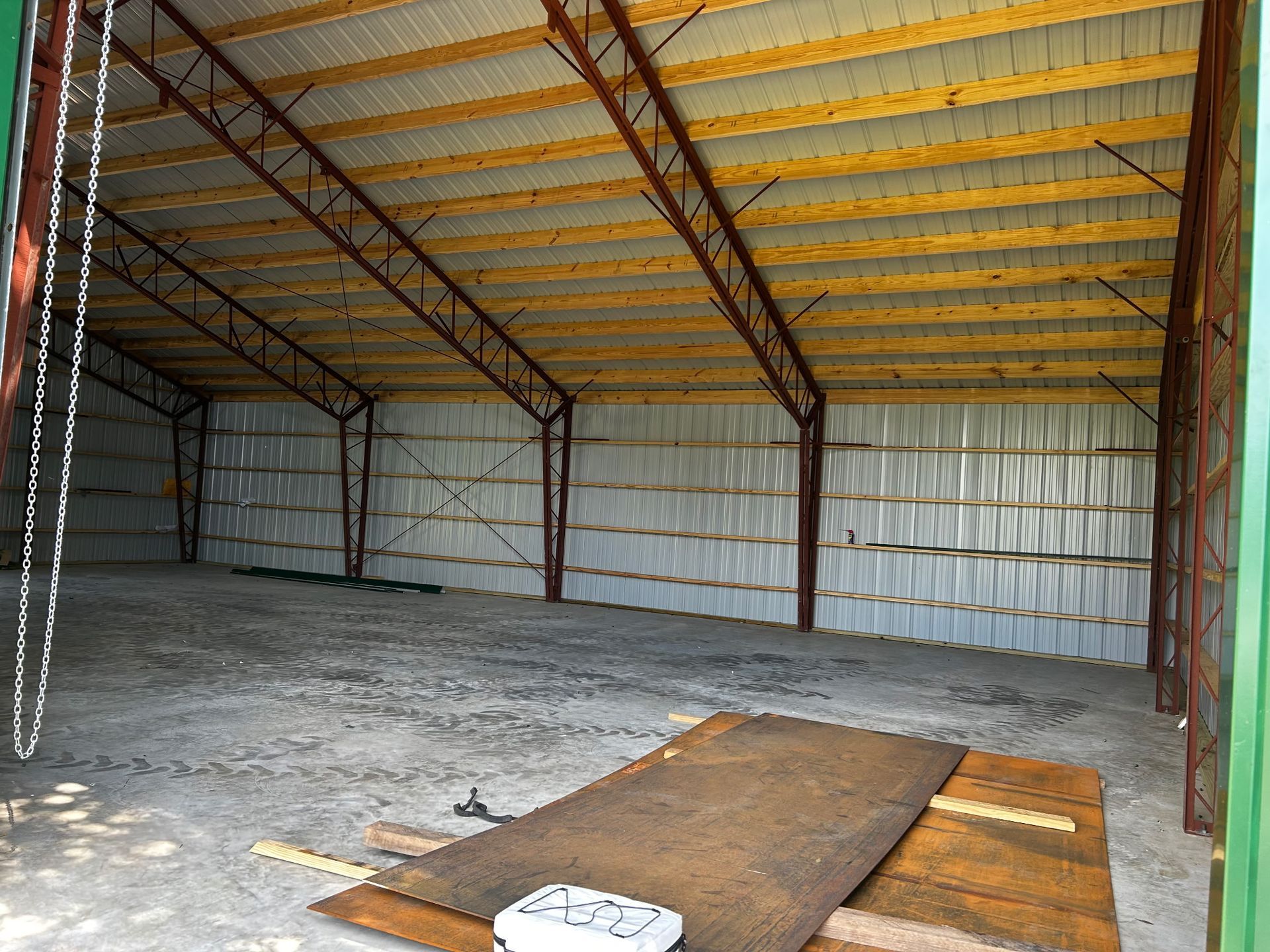 Interior of a large metal building with a concrete floor, wood roof supports, and corrugated metal walls.