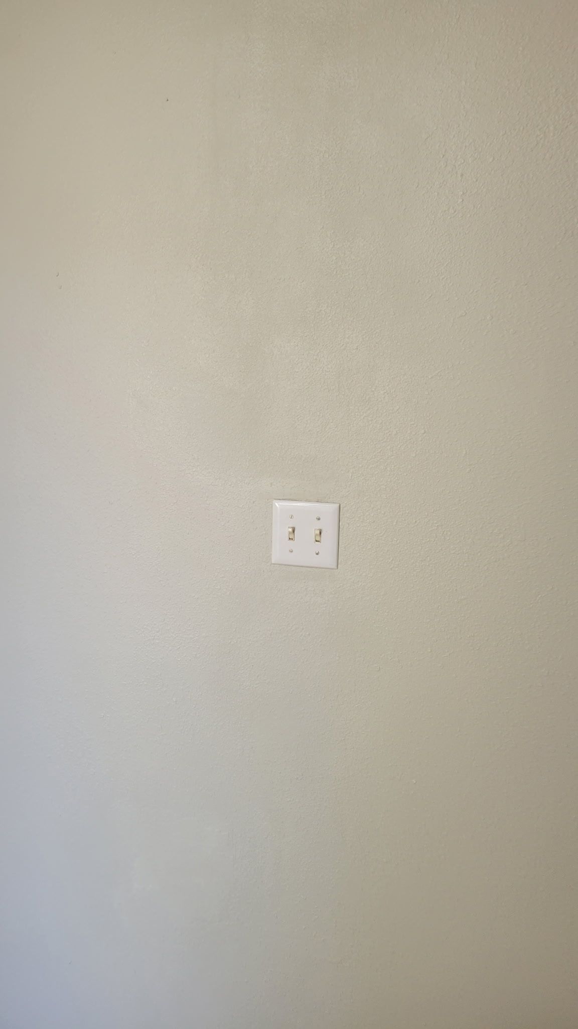 White wall with textured finish, centered electrical outlet with two receptacles.
