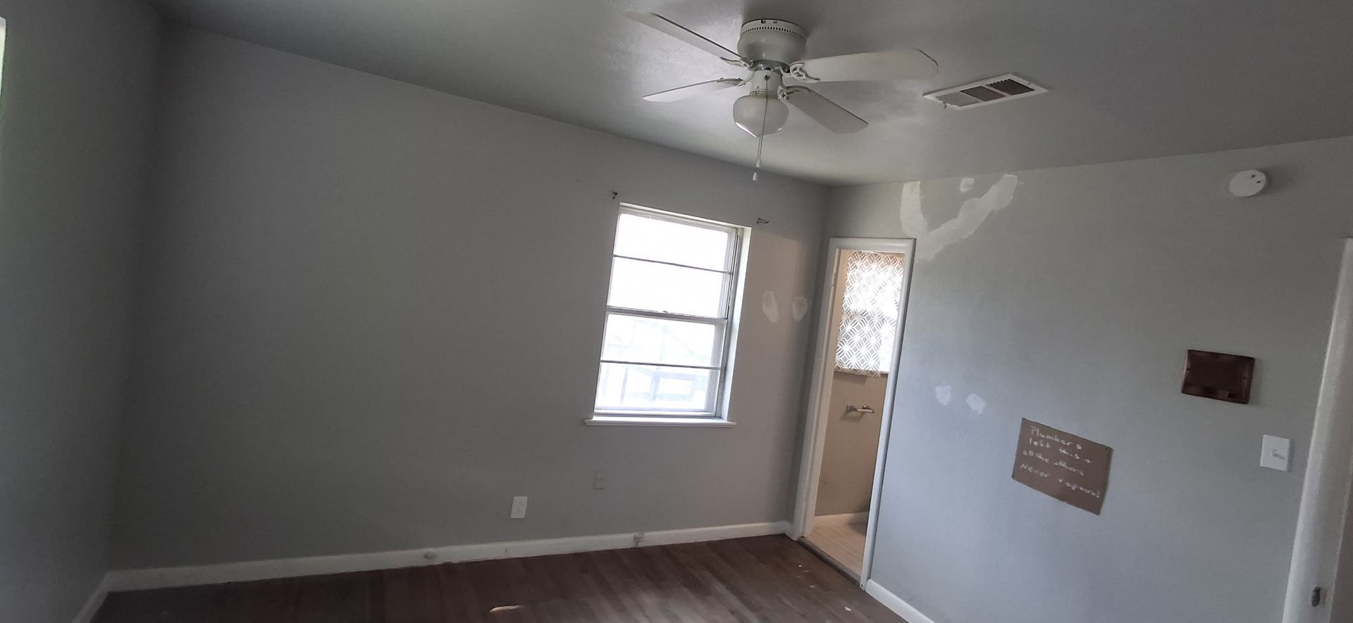 An empty room with gray walls and a ceiling fan, a window, and a doorway.