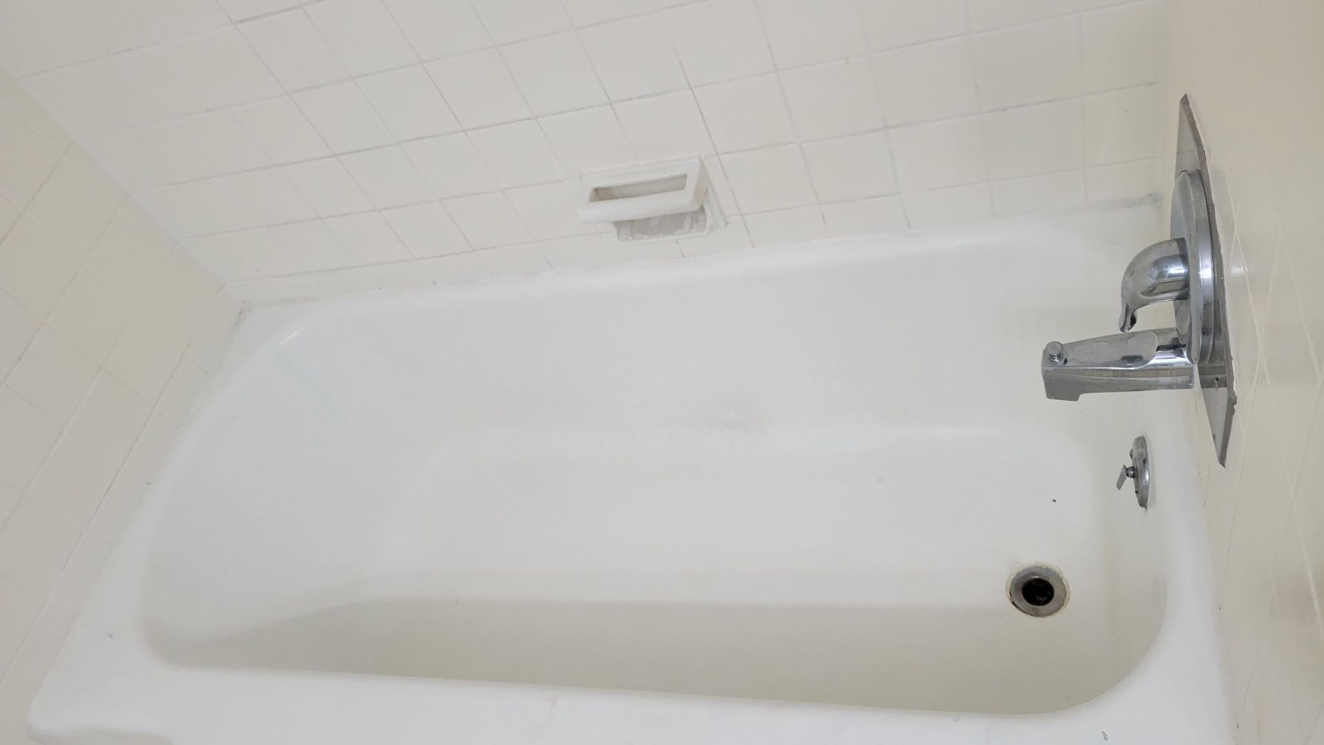 White bathtub with chrome shower fixtures and soap dish in a tiled bathroom.