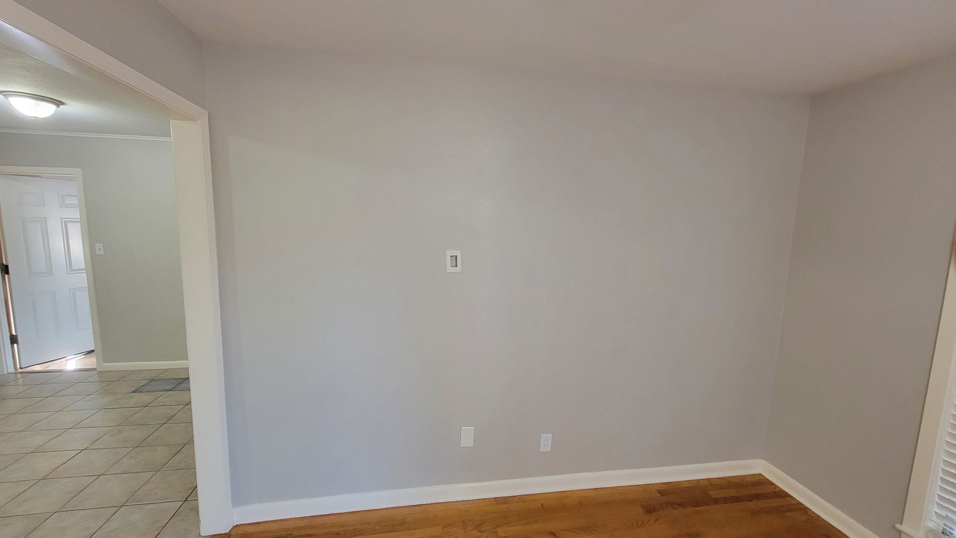 Empty room with light gray walls, white trim, and hardwood floor.