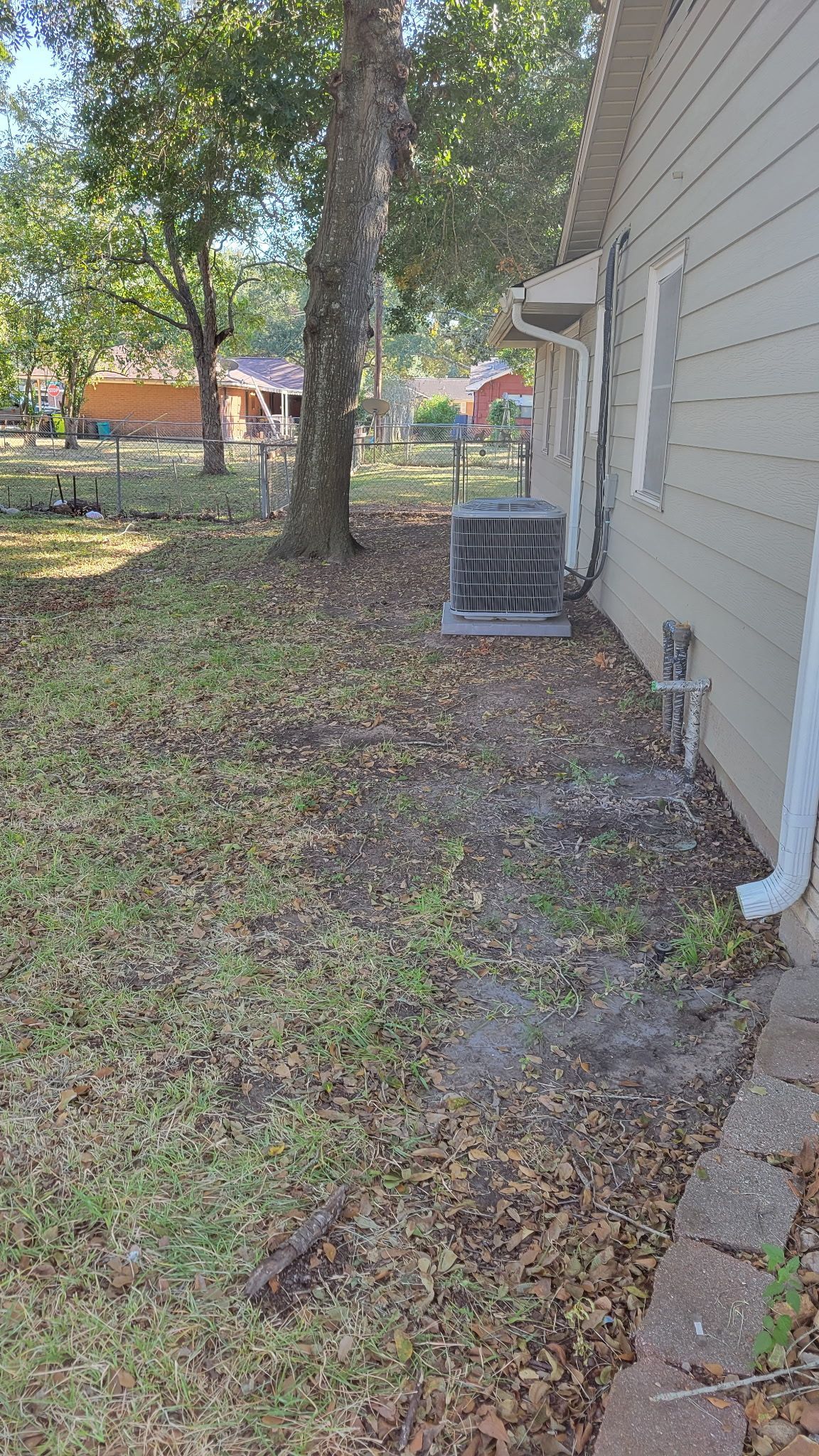 A side view of a house with an AC unit and a yard covered in leaves.