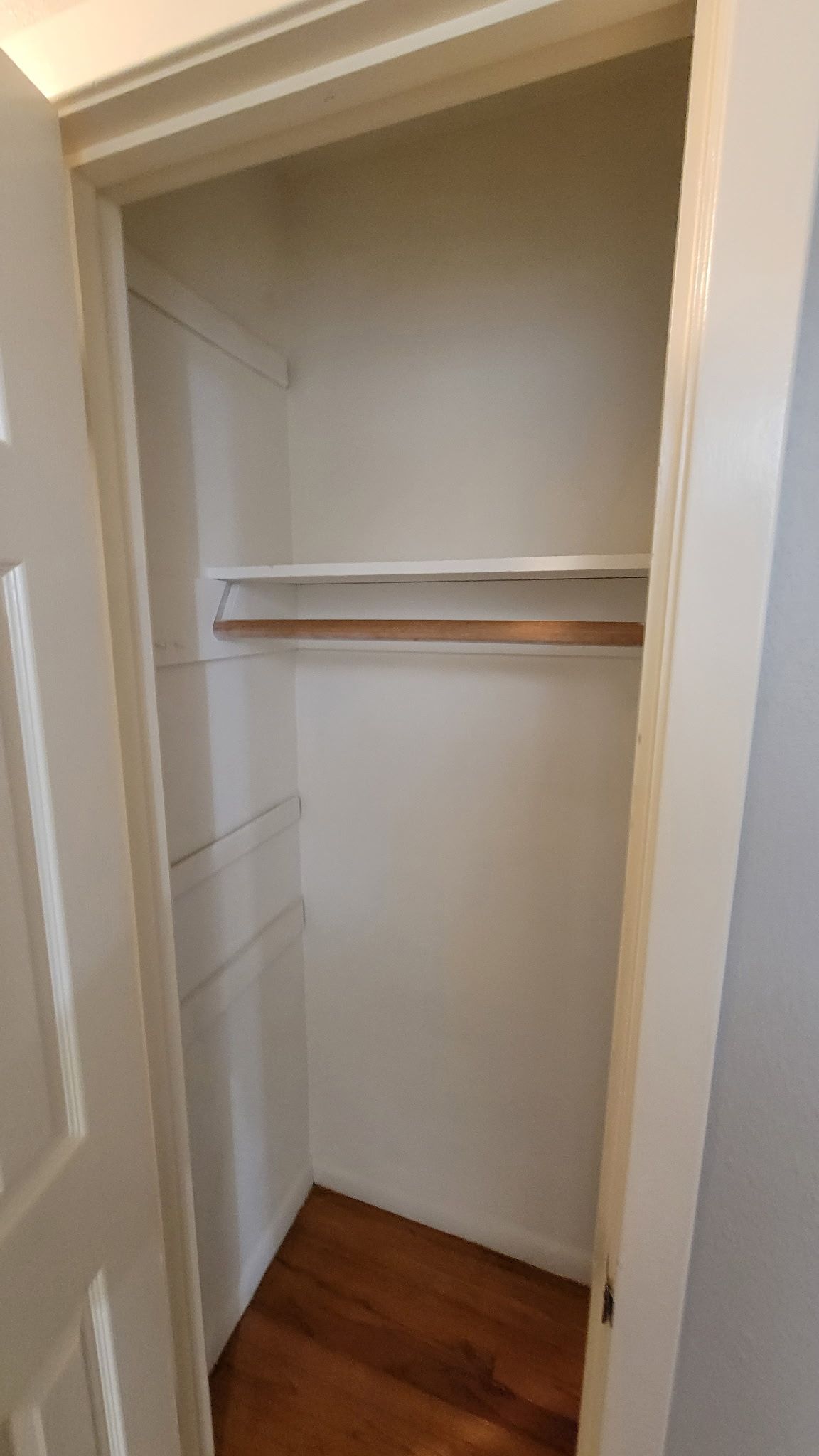 Empty white closet with wooden floor, rod, and shelves.