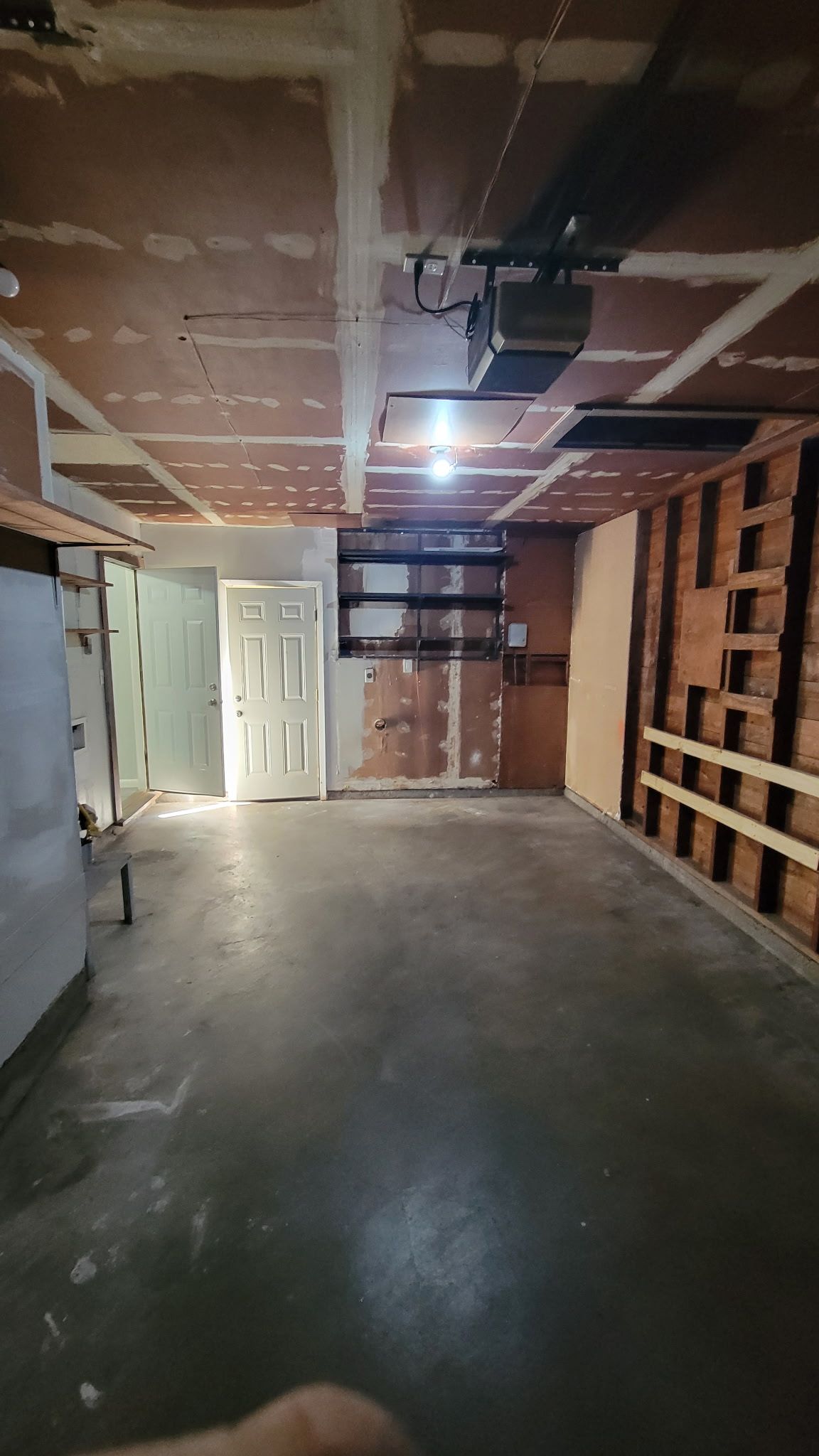 An unfinished basement with exposed brick and studs, concrete floor, white door, and overhead ductwork.