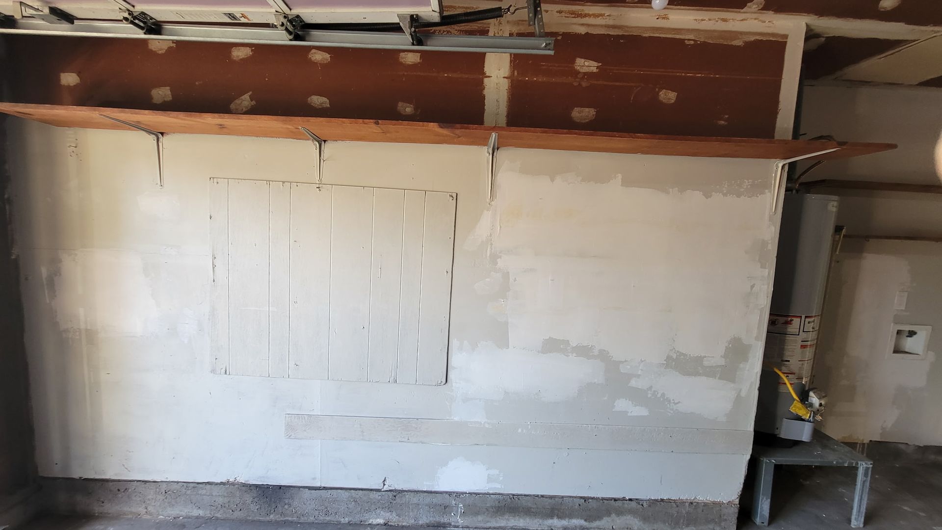 Garage interior with a partially constructed wall and wooden shelf.