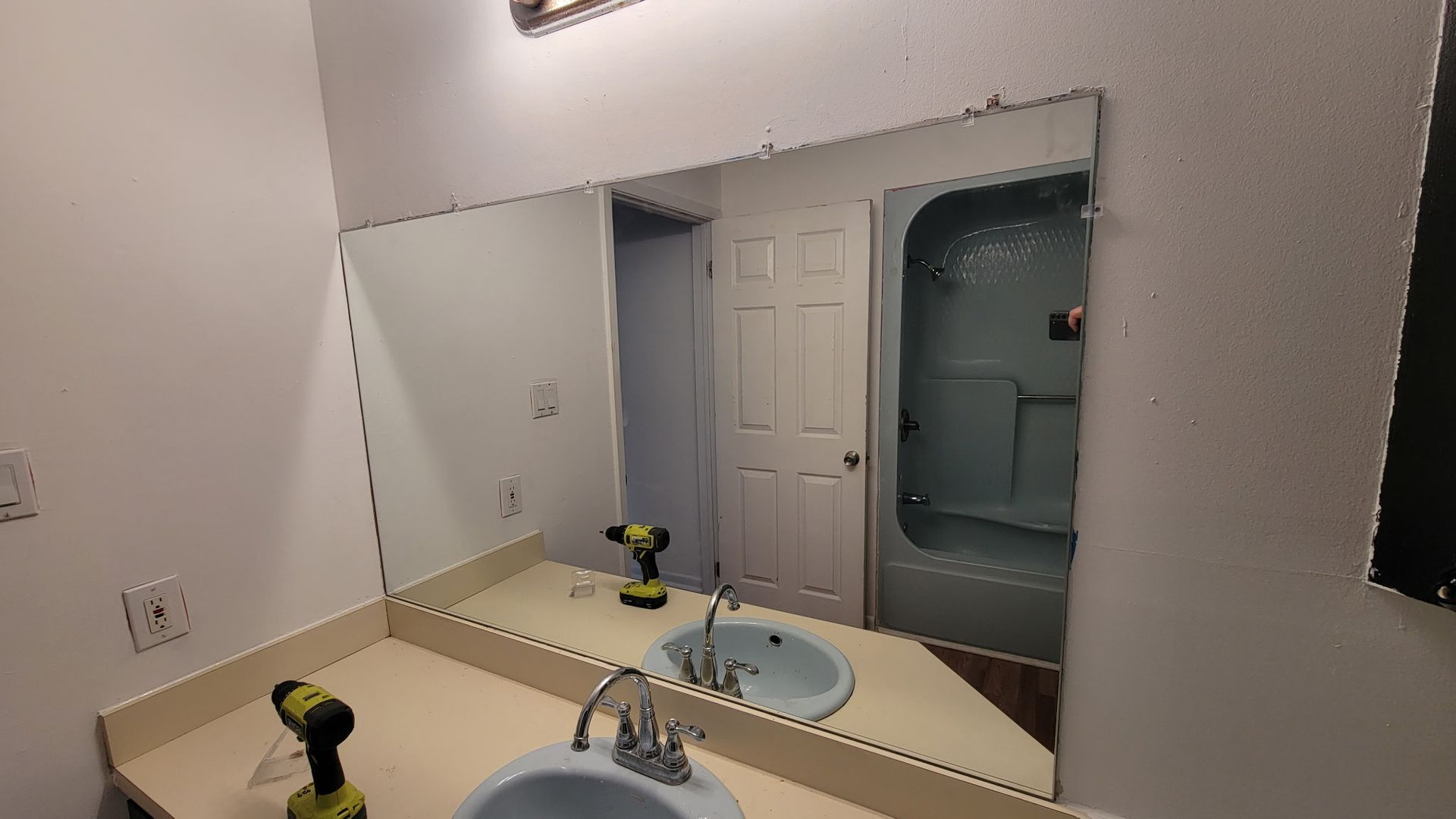 Bathroom mirror over a sink and countertop, showing a reflection of a shower and door.