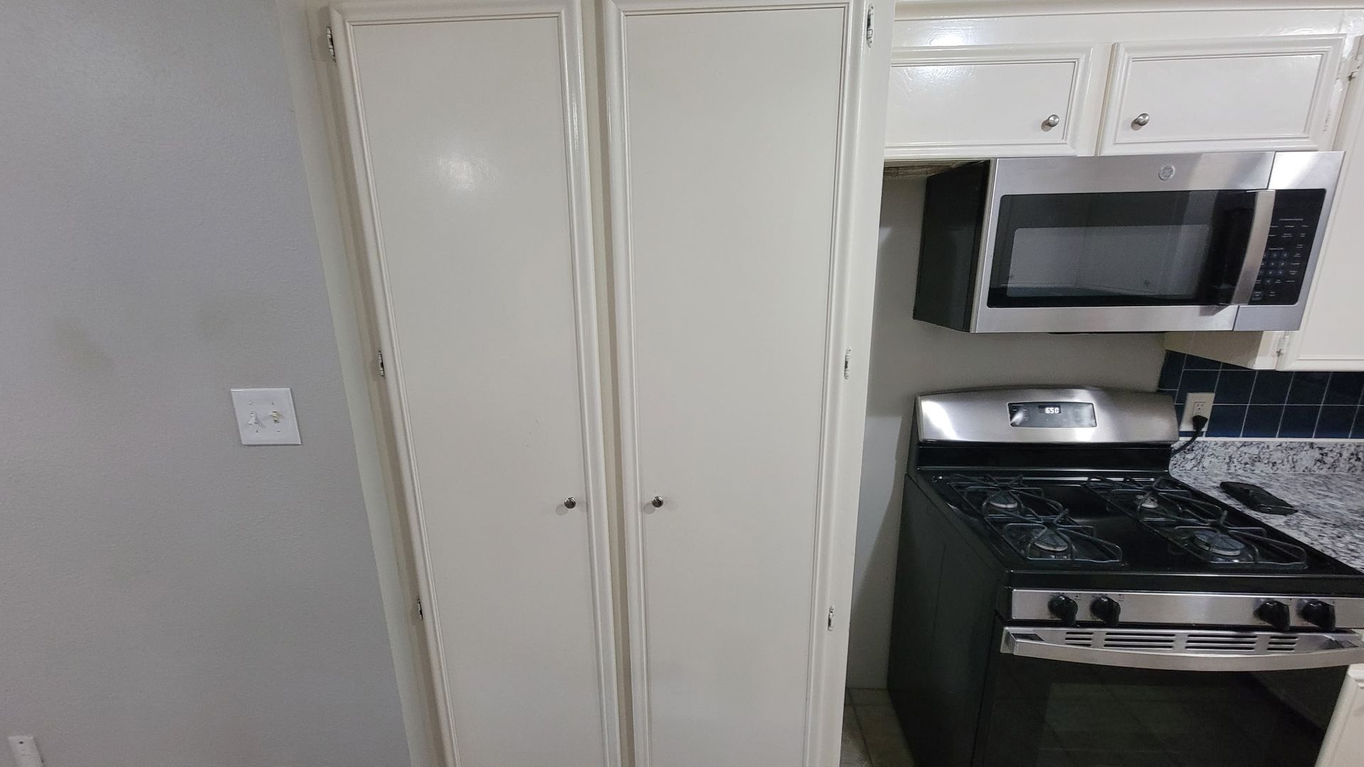 Kitchen with tall white cabinets, stainless steel microwave and gas stove, gray wall.
