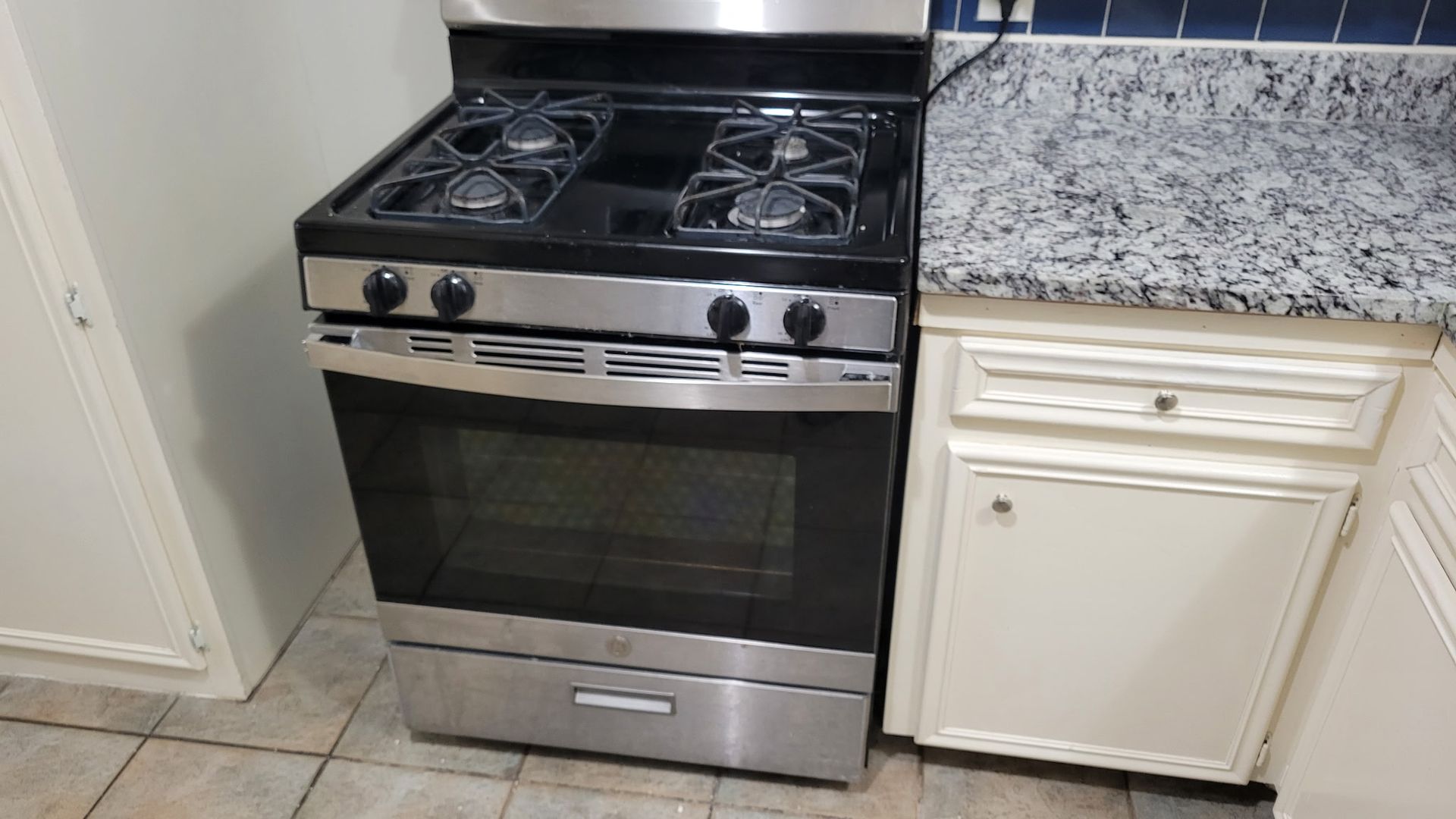 Stainless steel gas range in a kitchen next to a white cabinet with a granite countertop.