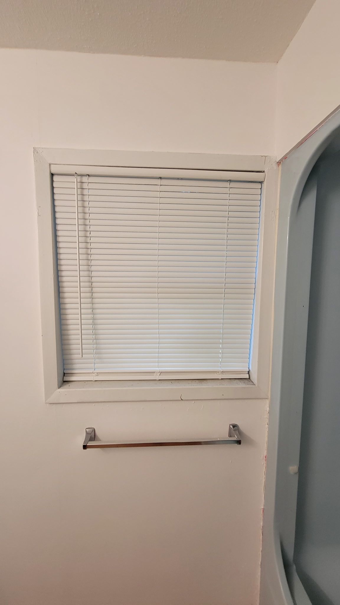 Window with white blinds in bathroom; towel rack below.