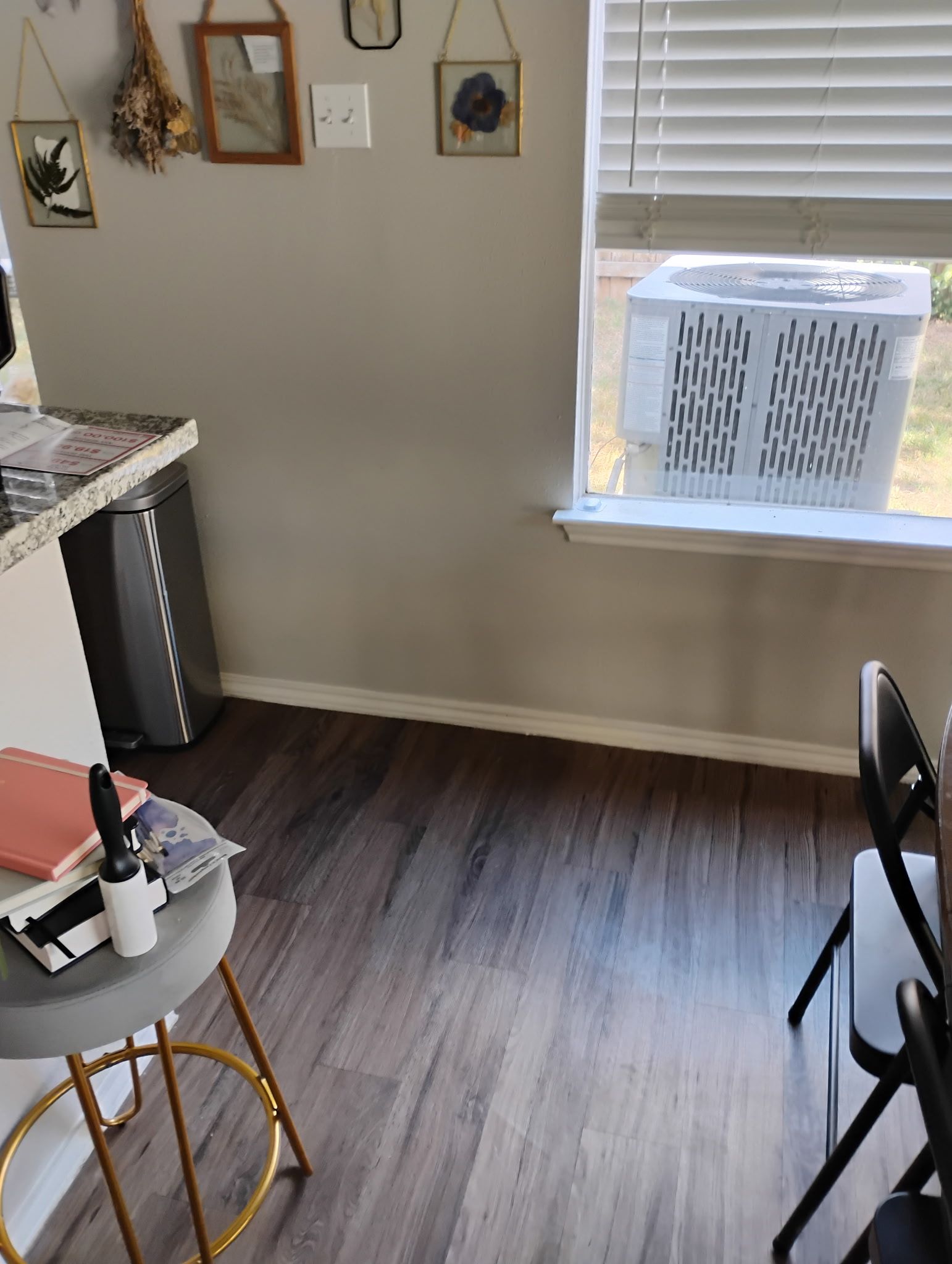 Interior room with air conditioner in window, stool, countertop and dark wood floor.