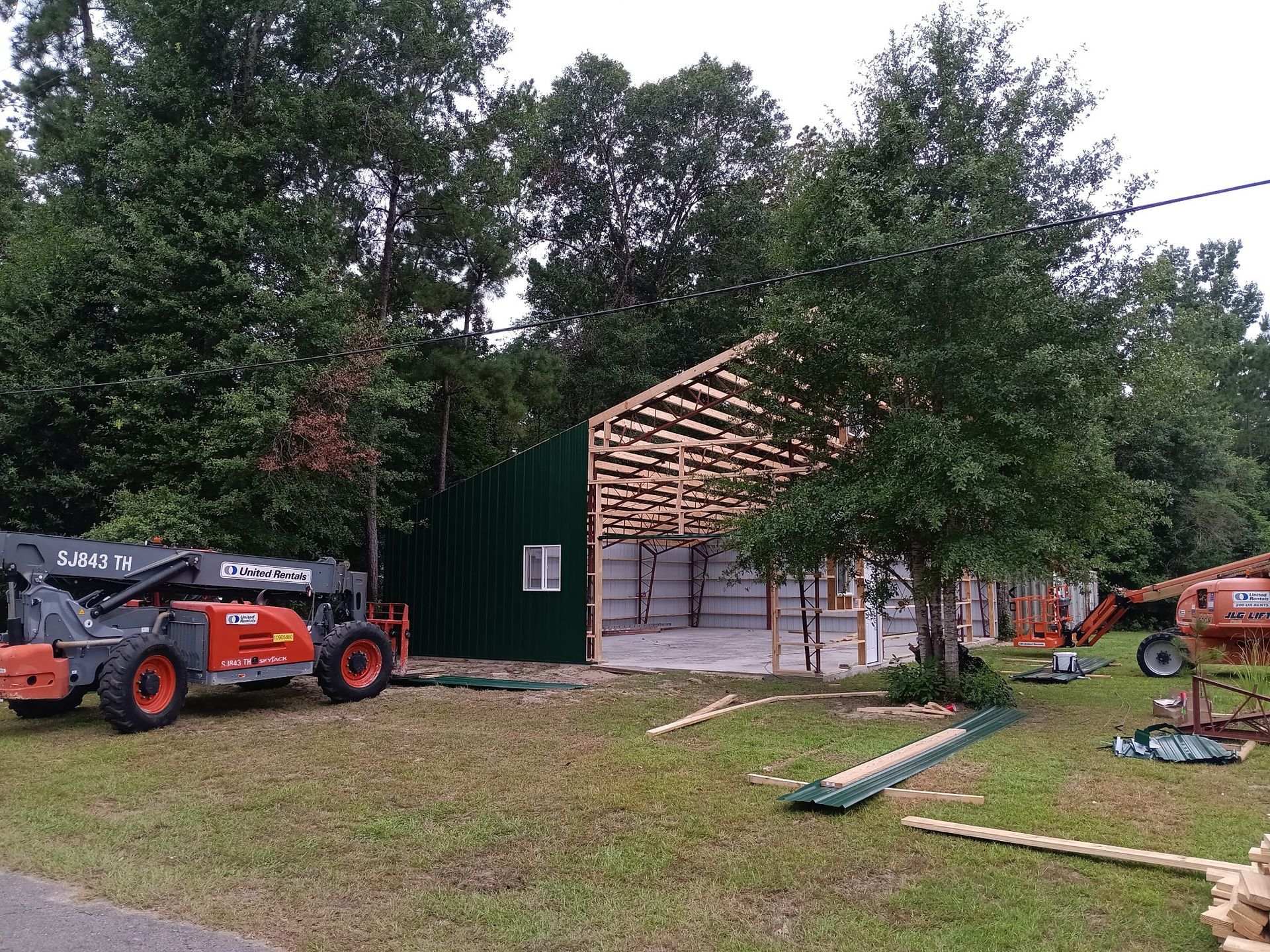 Construction of a green-sided building with exposed rafters; heavy equipment nearby.