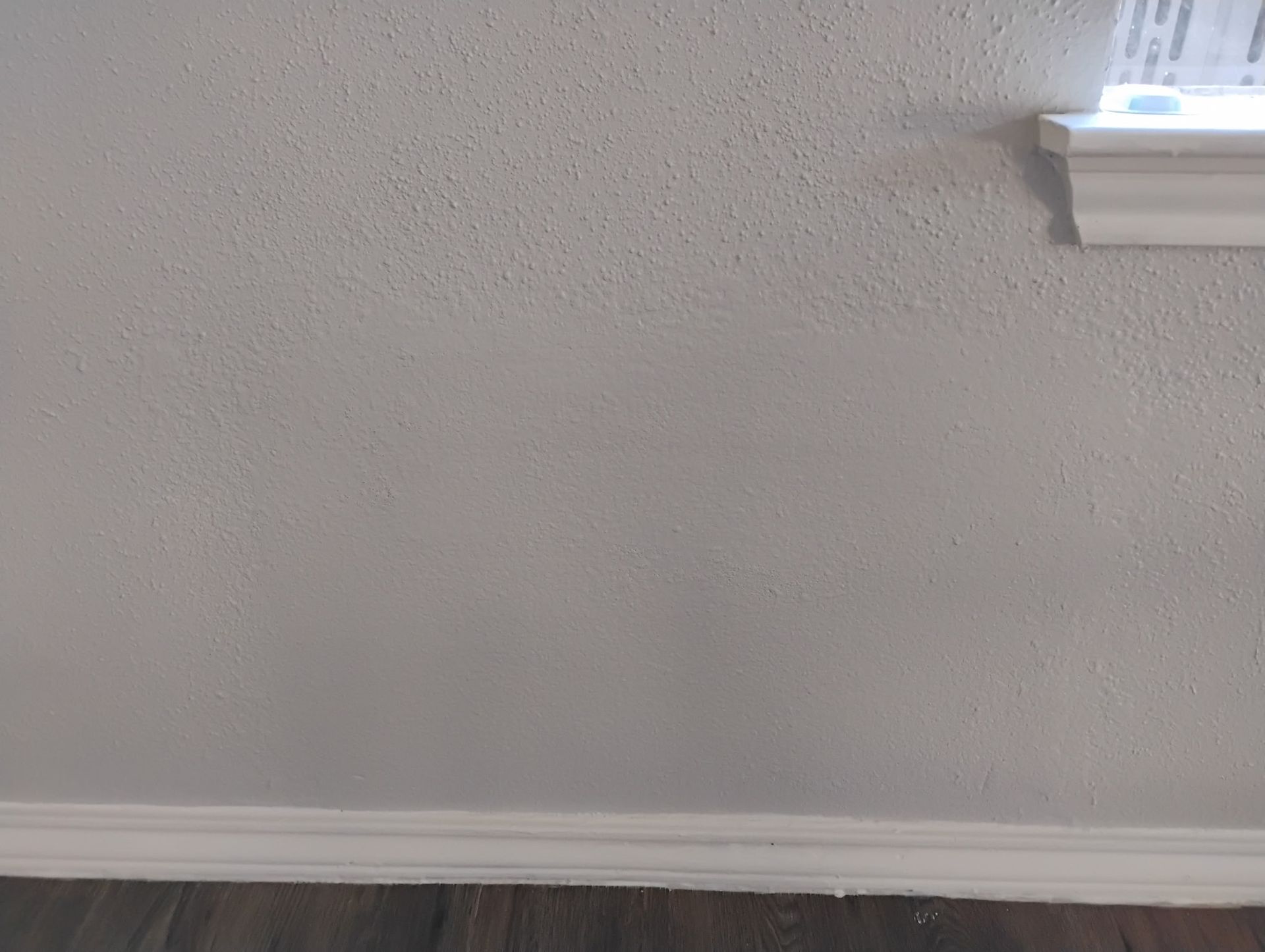 Gray textured wall with white baseboard and window trim. Dark wood floor visible.