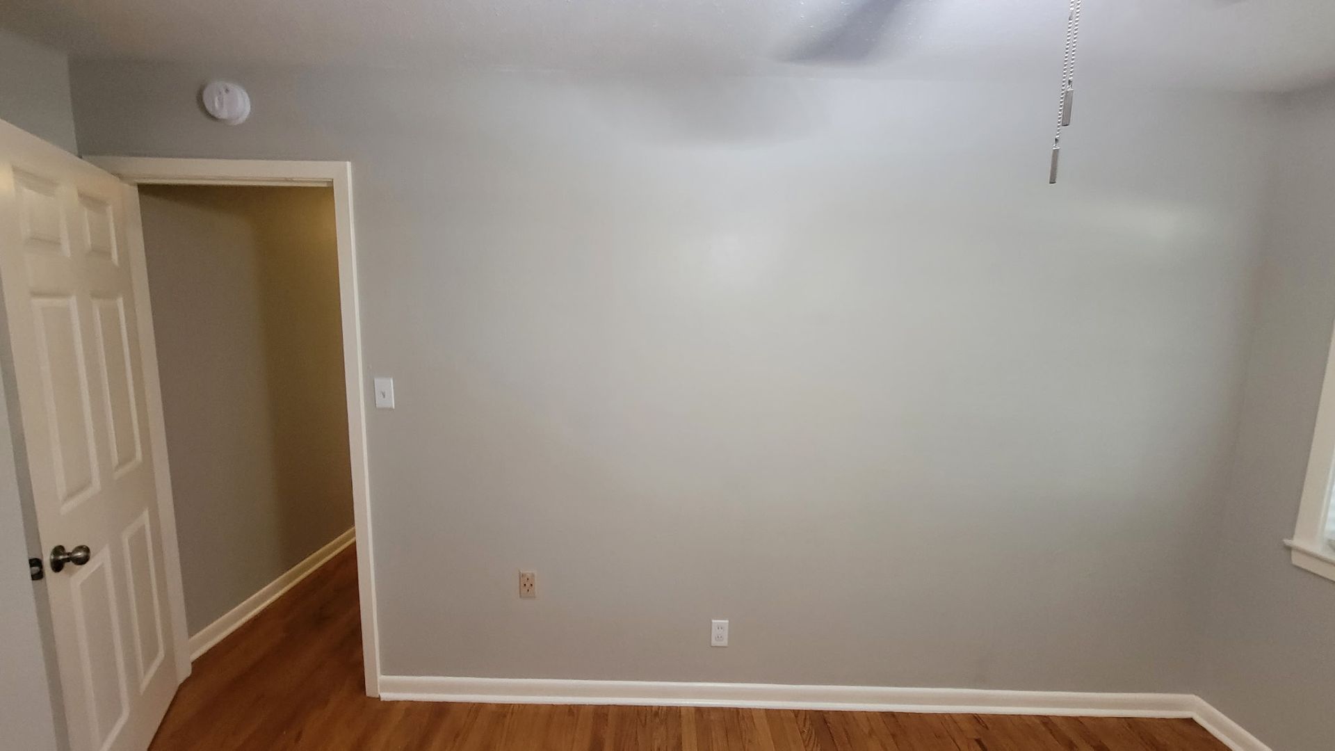 Empty bedroom with gray walls, wood floor, and an open doorway.