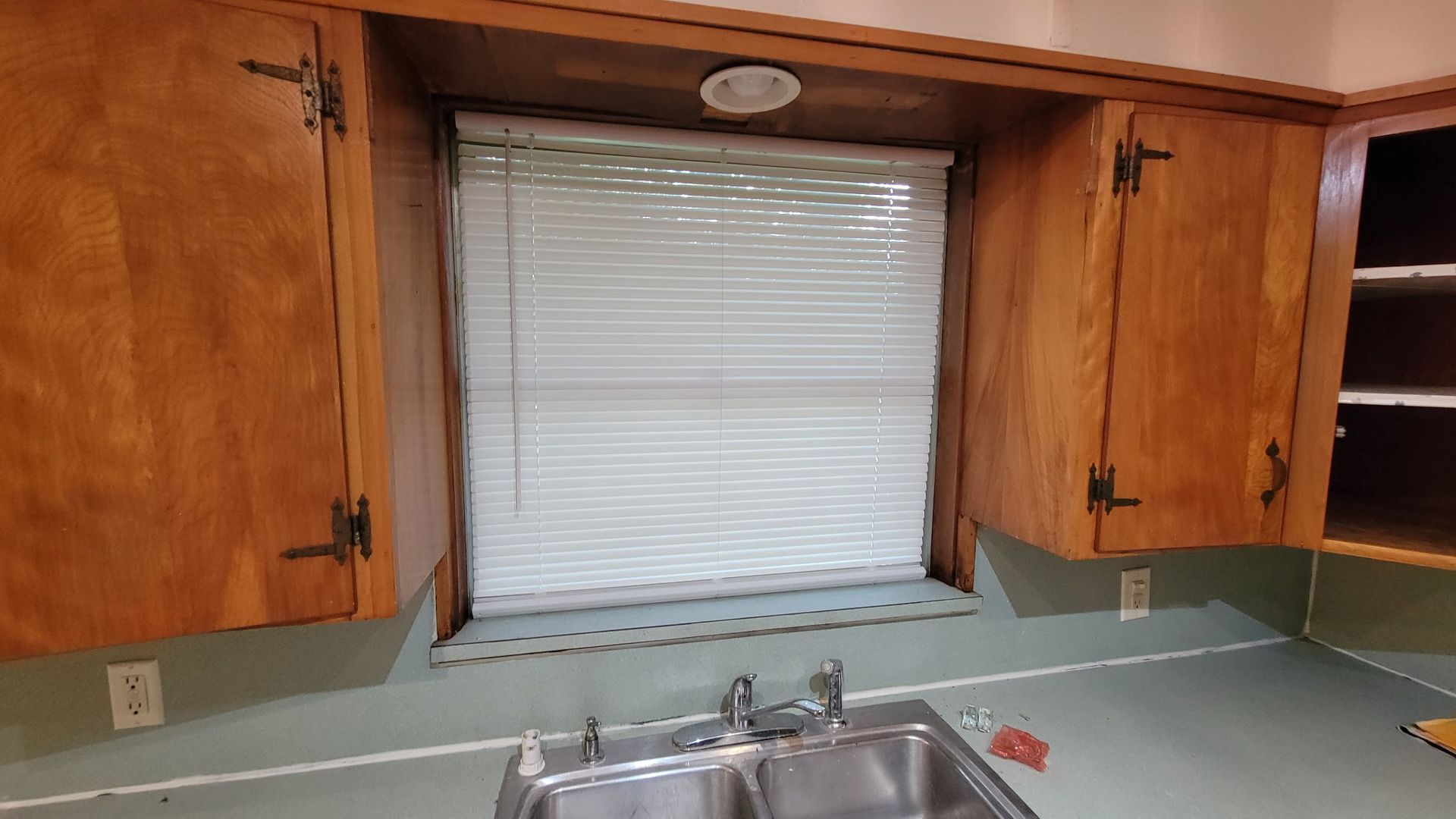 Kitchen with wooden cabinets, window with blinds, and a stainless steel sink.
