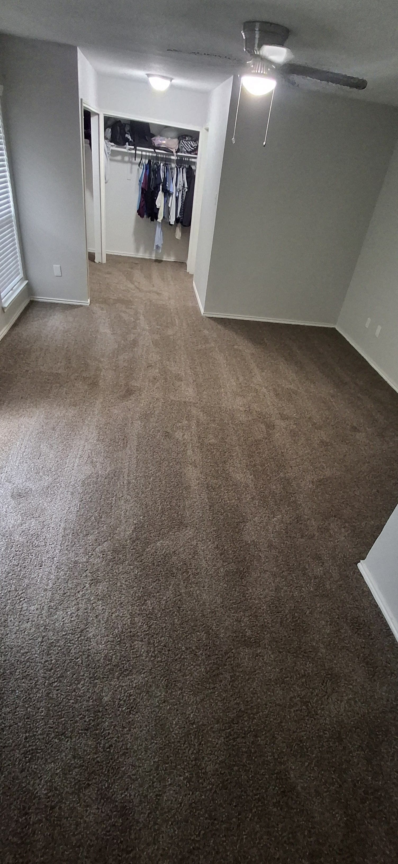 A room with brown carpet, white walls, and a closet at the end. A ceiling fan is visible.