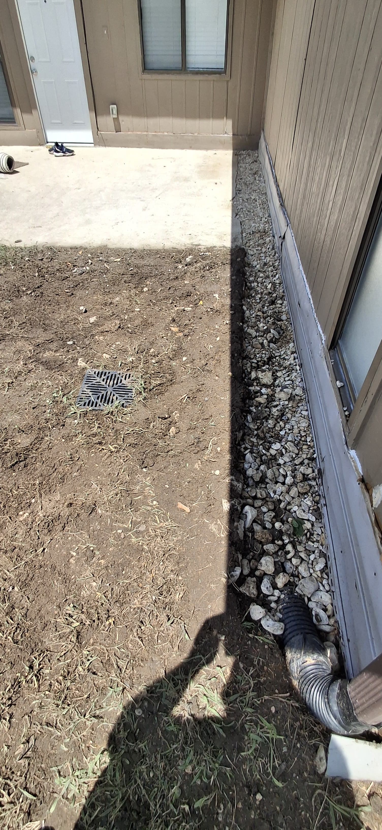 A gravel-filled trench next to a building, with a shadow of a person in the foreground.