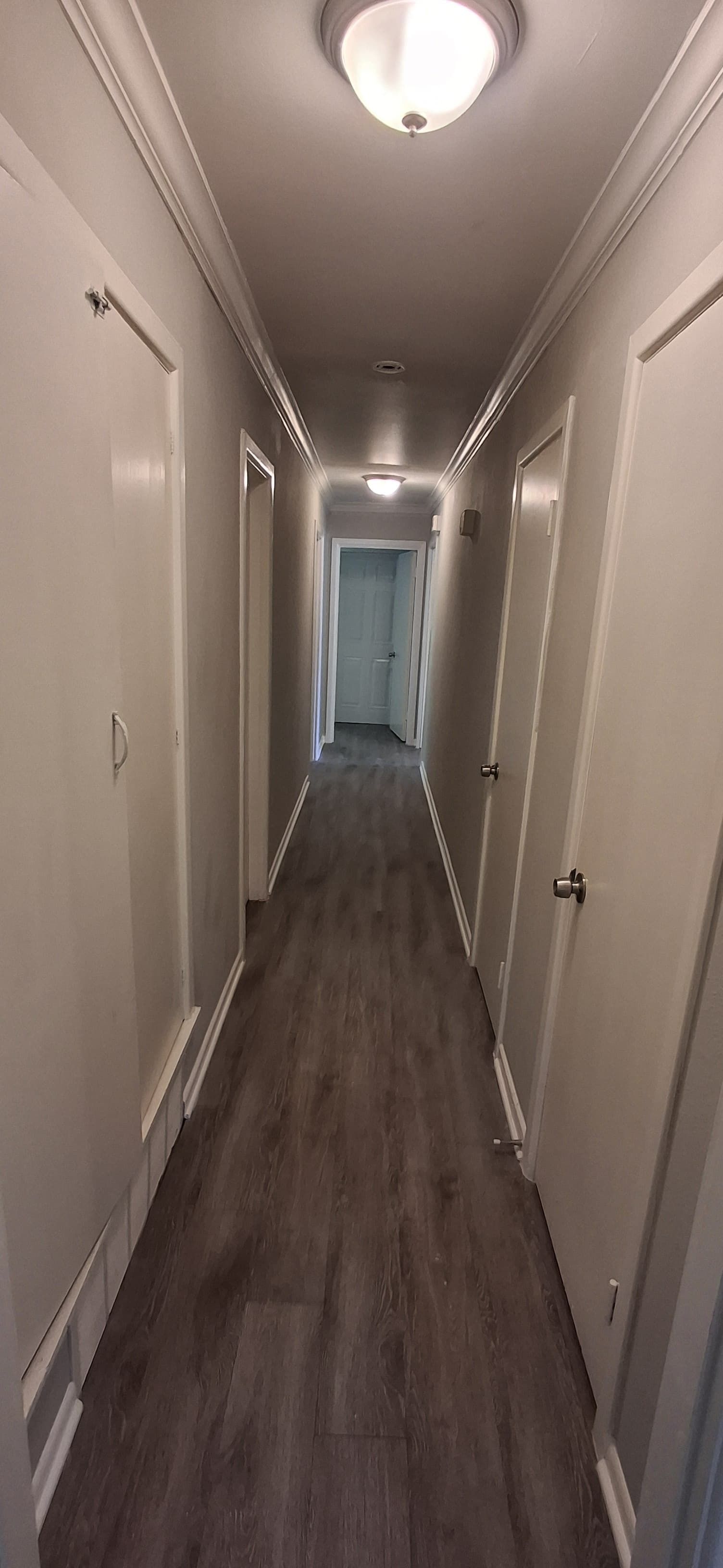 Narrow hallway with doors on both sides and a light at the end of the hallway.
