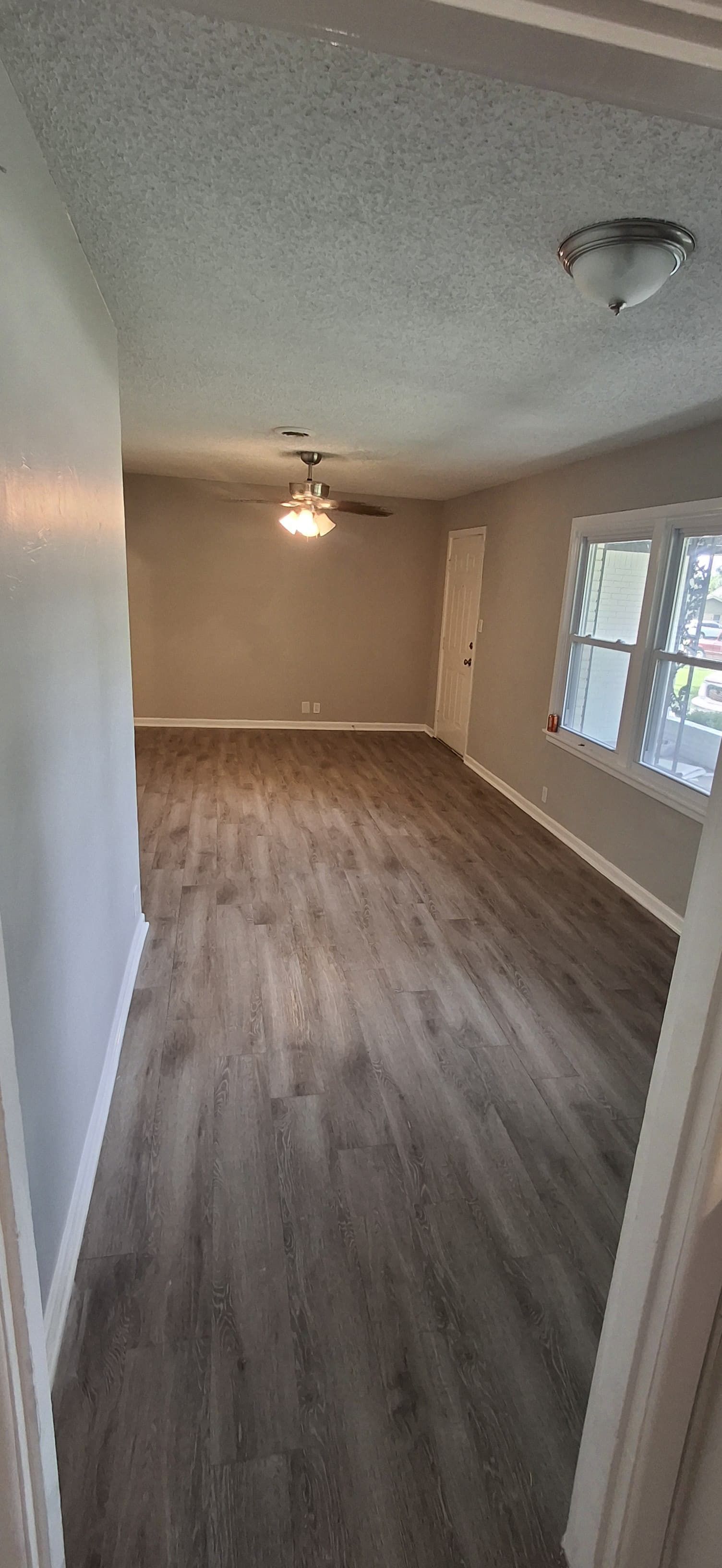 A room with gray laminate flooring, gray walls, white trim, and a ceiling fan.