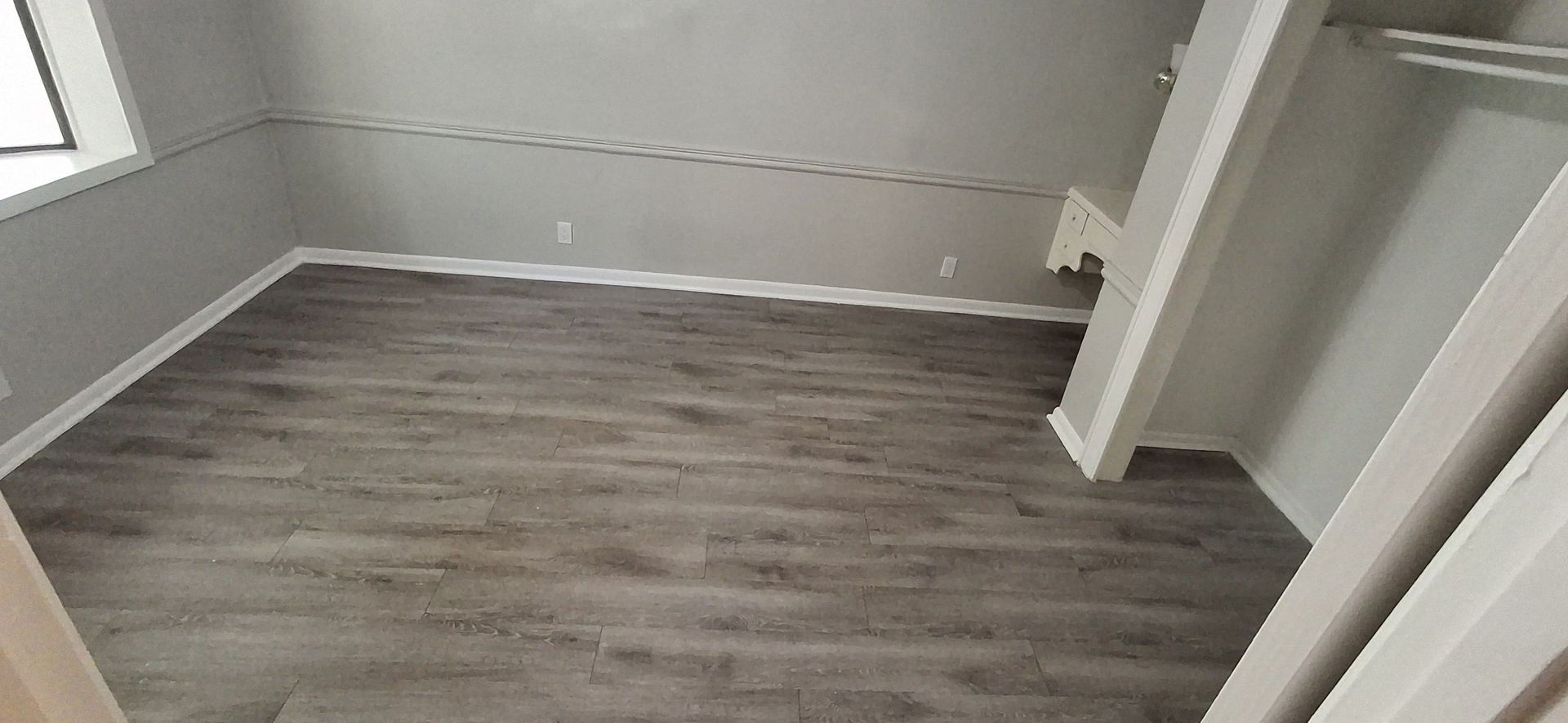 Empty room with gray walls and wood-look flooring. White trim and closet structure.