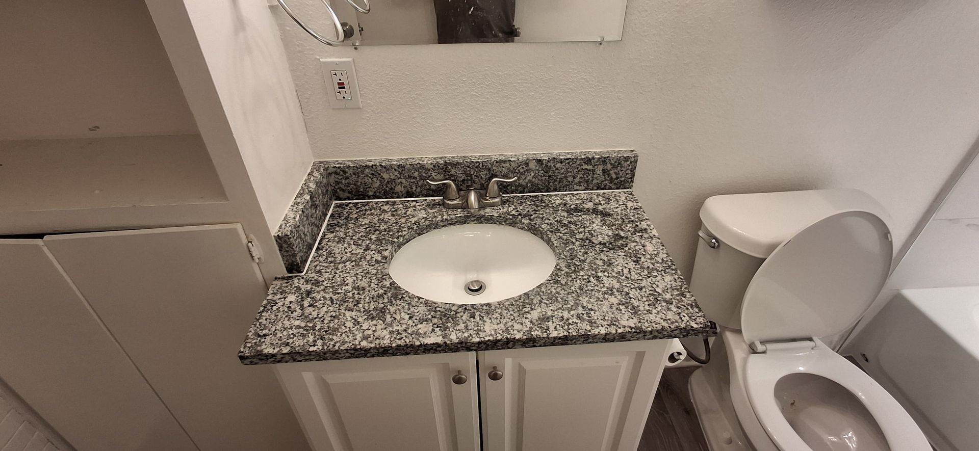 A bathroom with a sink and toilet. The sink has a granite countertop and the toilet seat is up.