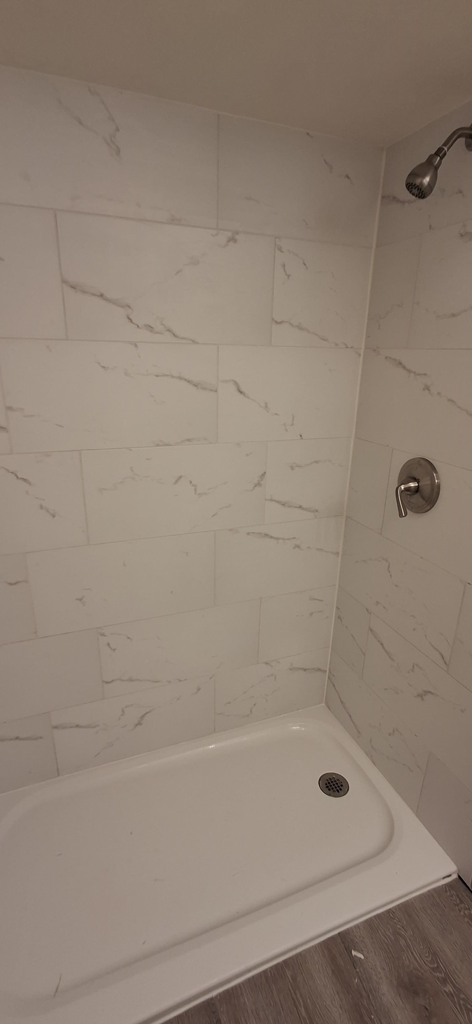 A white shower with marble-like tile walls, a white shower base, and silver fixtures.