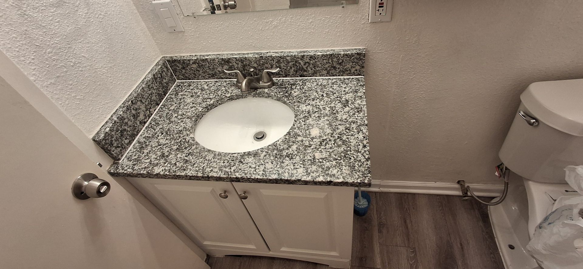 Bathroom vanity with white cabinet, granite countertop, and oval sink. Toilet is next to it.