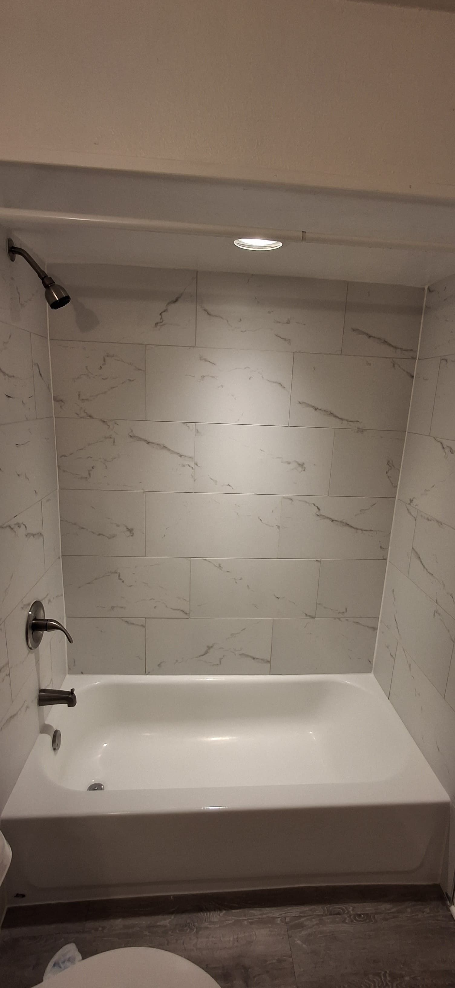 White bathtub and shower with white marble-like tile walls. Chrome showerhead and fixtures.