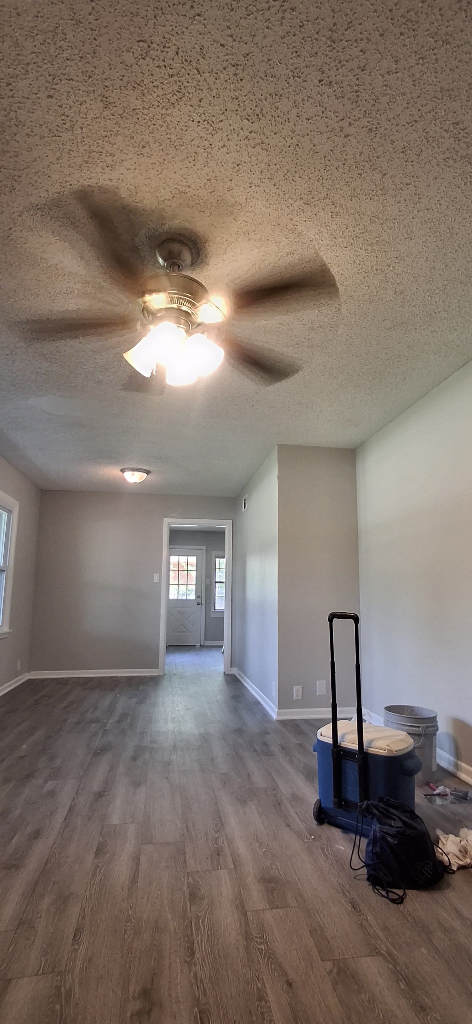 A room with gray walls and a ceiling fan, with a dark wood-like floor.