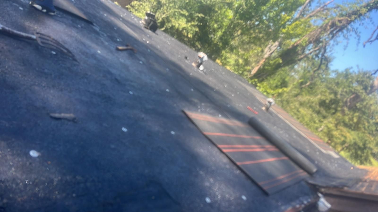 Dark, weathered roof with missing tiles. Sunlight shines through trees in the background.