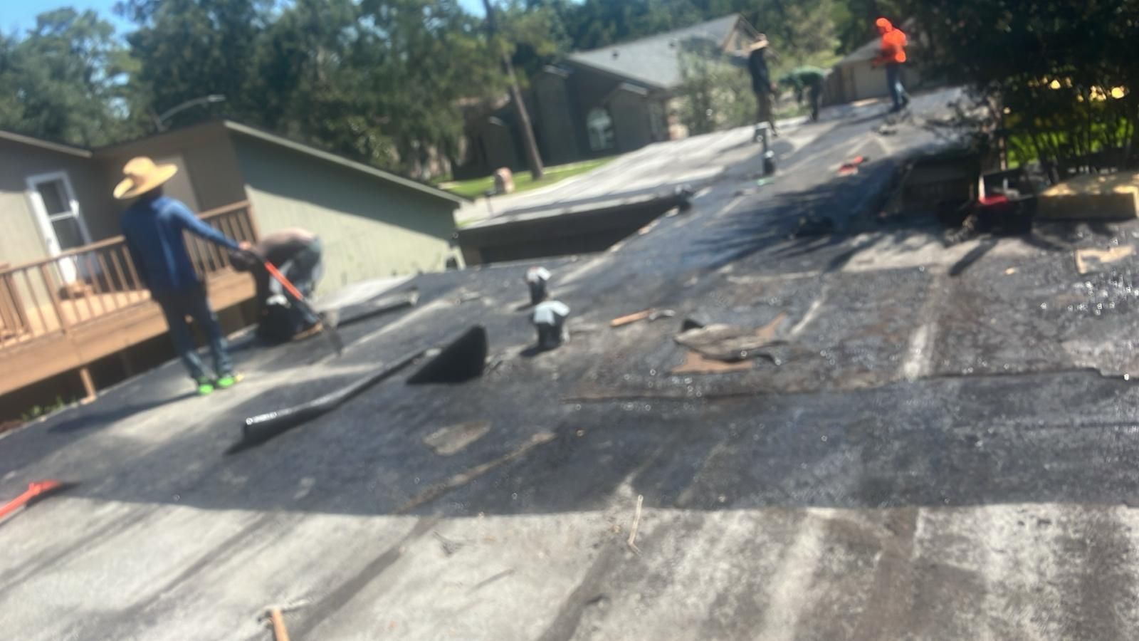 Workers on a rooftop removing old roofing material from a residential building.