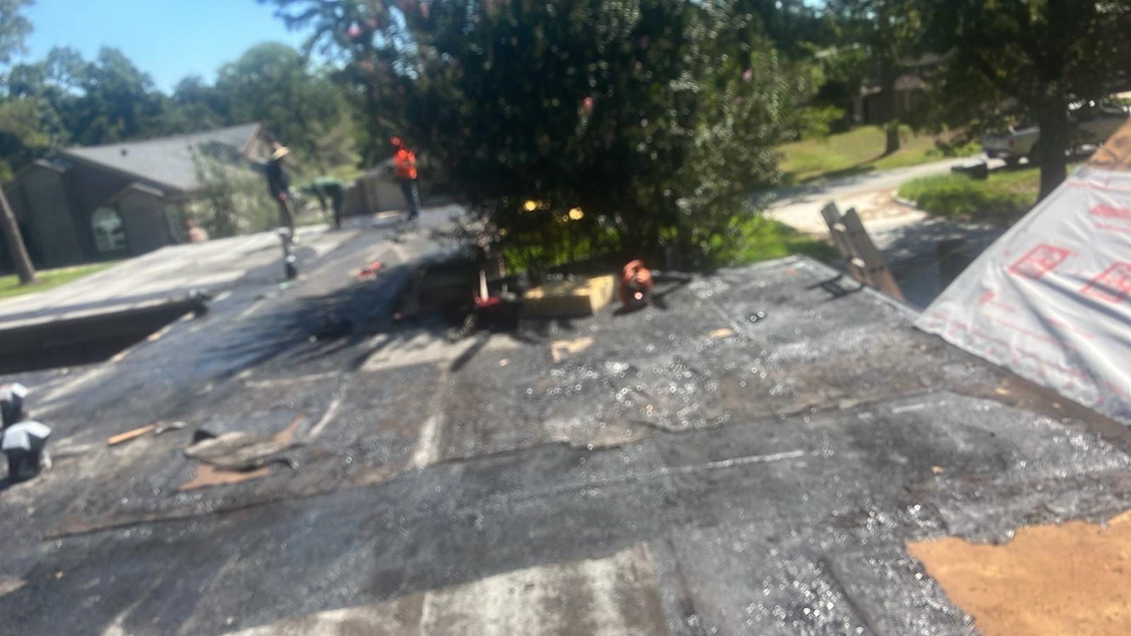 Roofers working on a damaged roof, debris scattered, sunny day, residential setting.