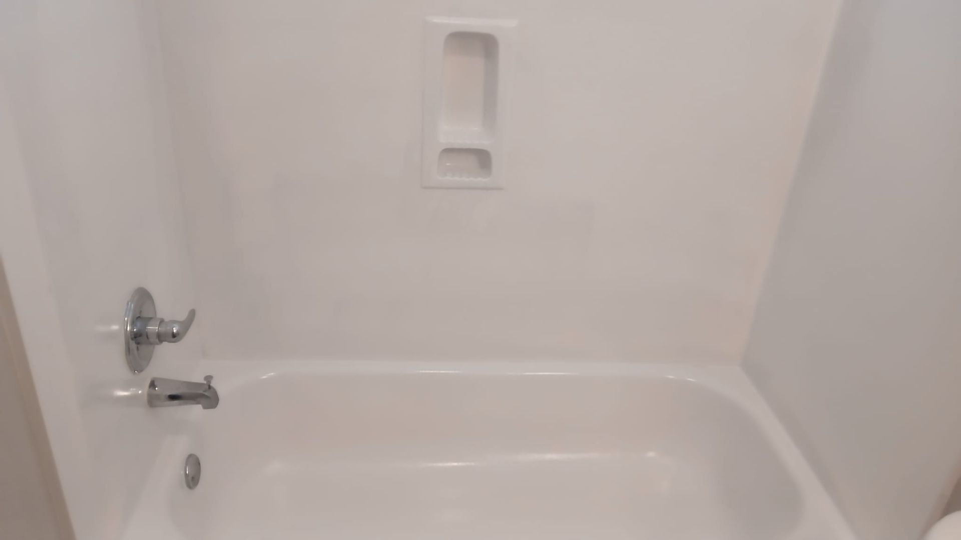 Empty white bathtub with faucet and built-in soap dish in a bathroom.